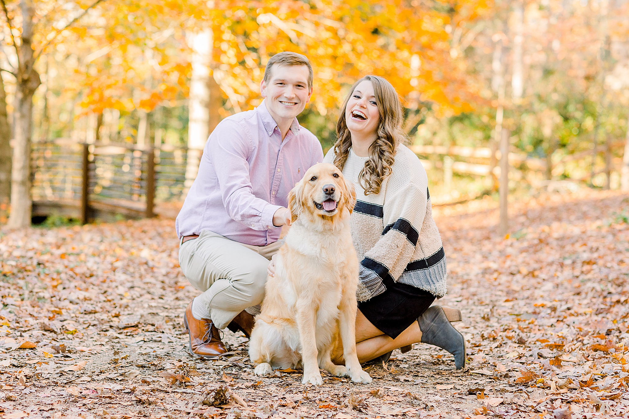 engaged couple kneels on leaves with golden retriever