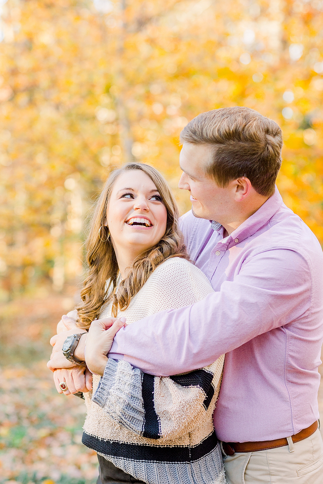 groom whispers in bride's ear during fall engagement photos