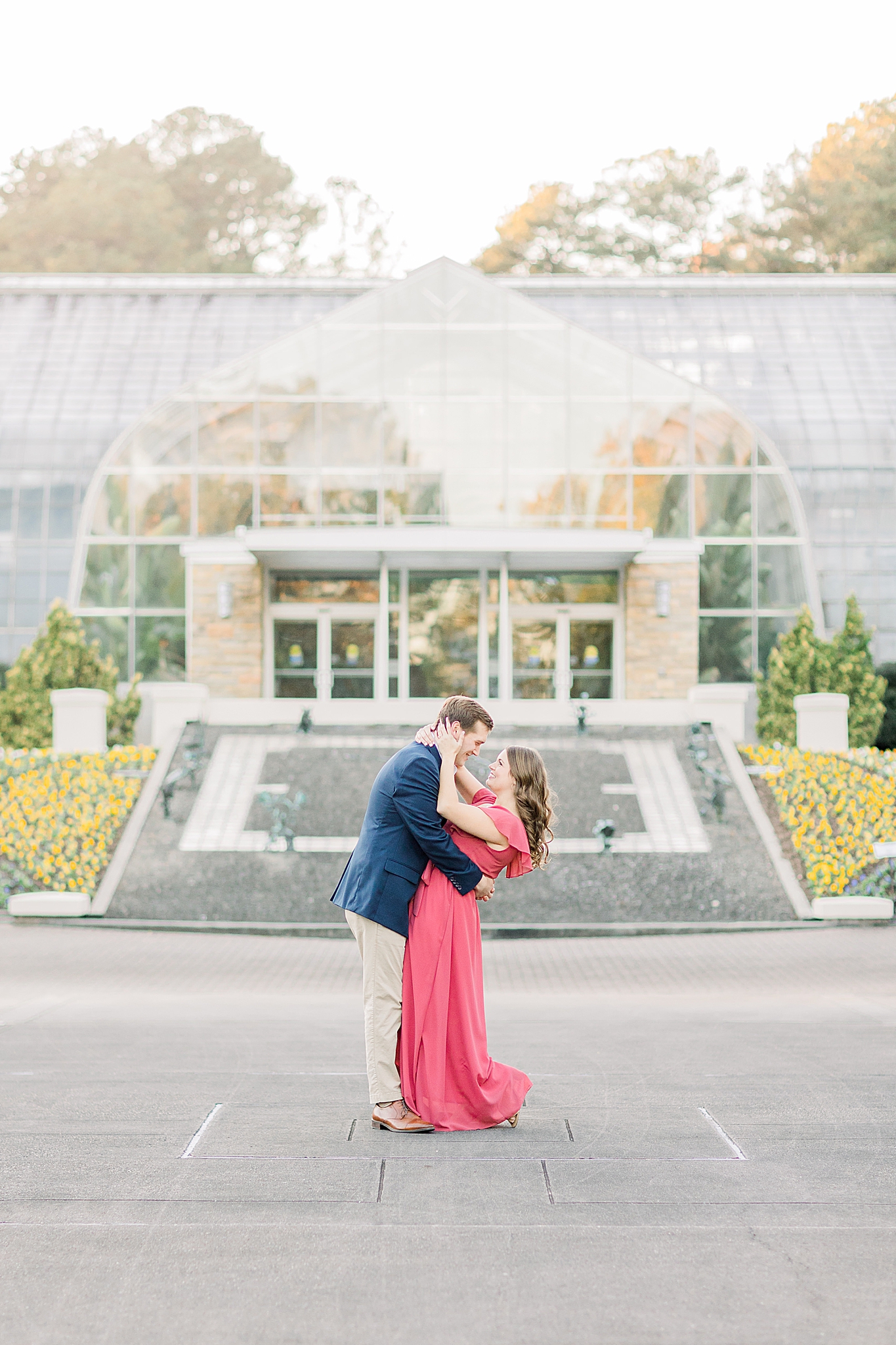engaged couple poses with noses touching in front of Birmingham Botanical Gardens