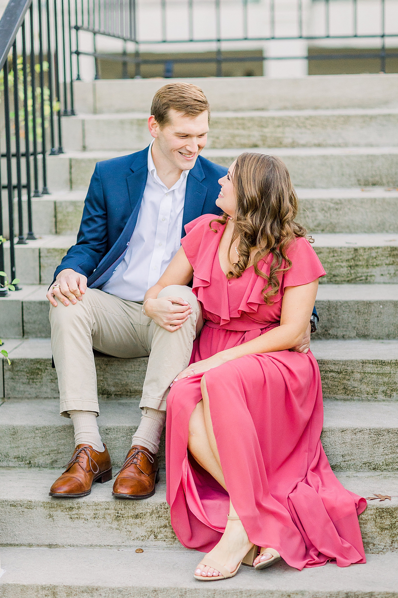 groom in navy jacket sits on steps with bride in coral dress at Birmingham Botanical Gardens
