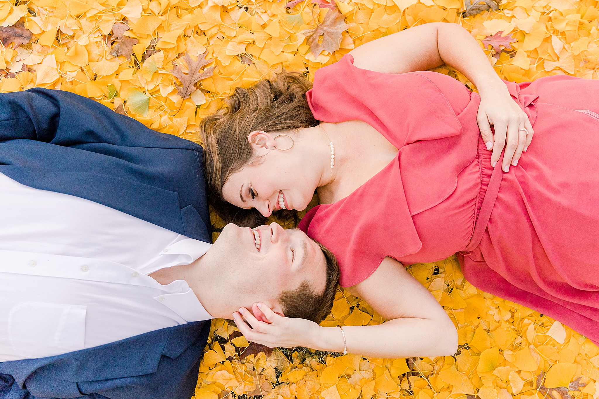 groom in navy jacket lays in yellow leaves with bride in coral dress