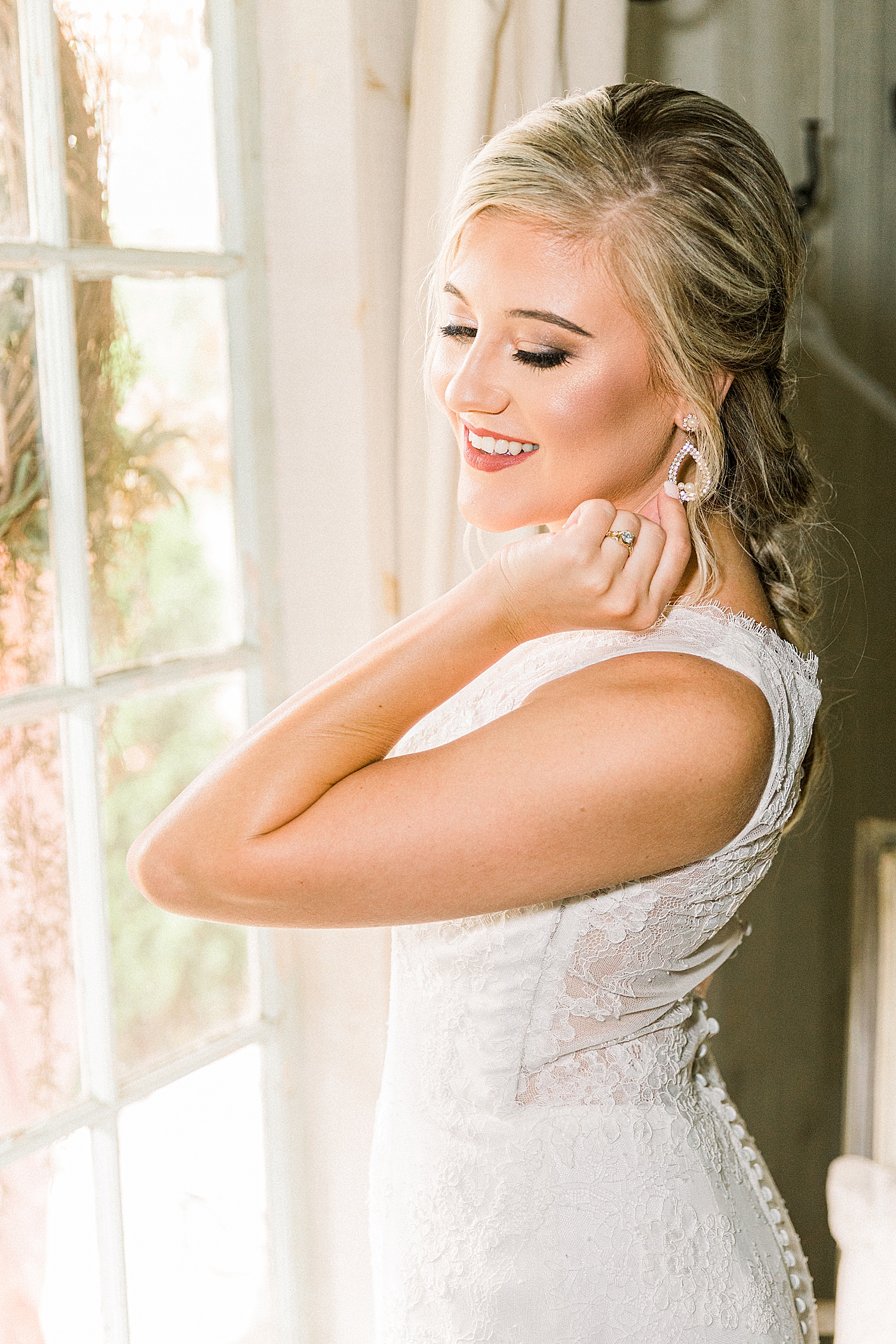 bride adjusts earrings looking out window at Creekside Meadows
