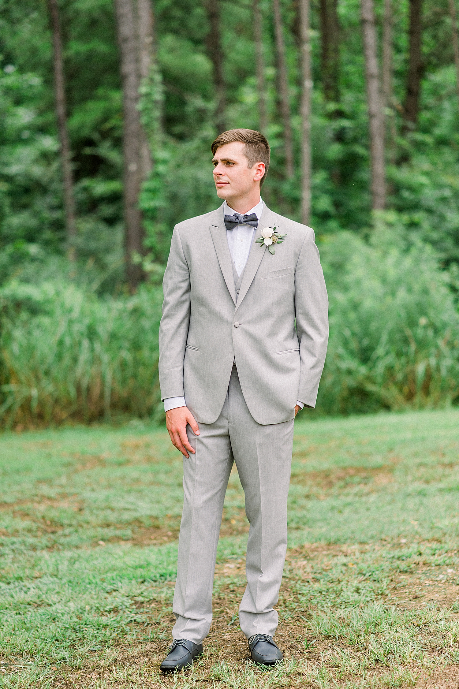 groom in grey suit looks over shoulder at Creekside Meadows