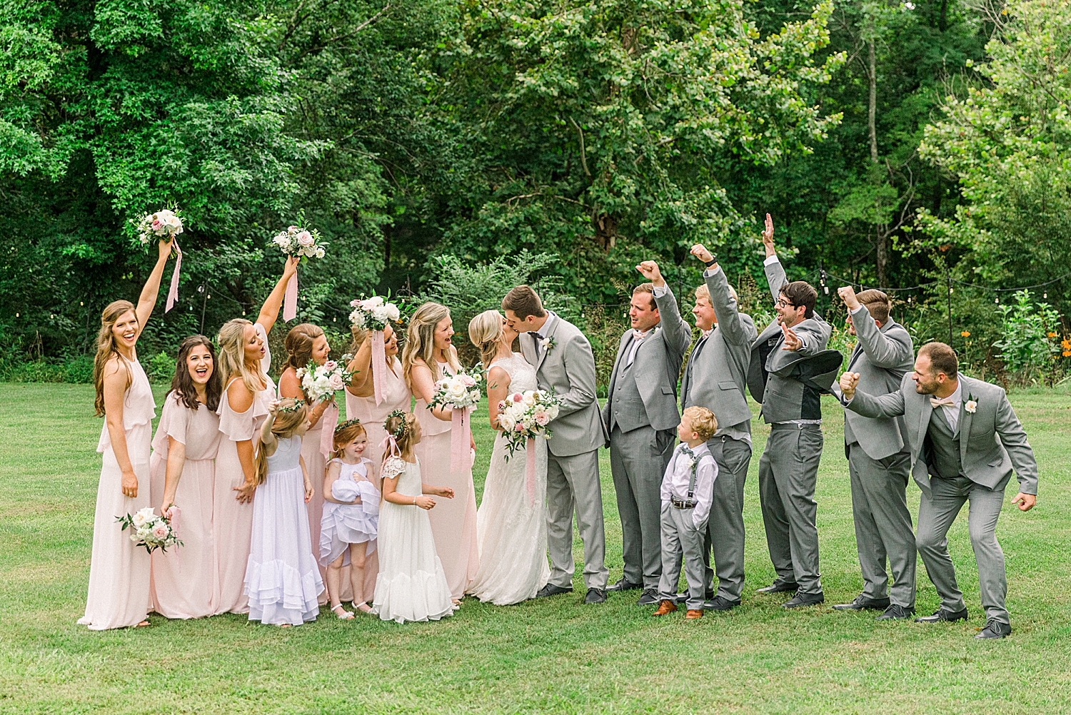 bridal party cheers while newlyweds kiss