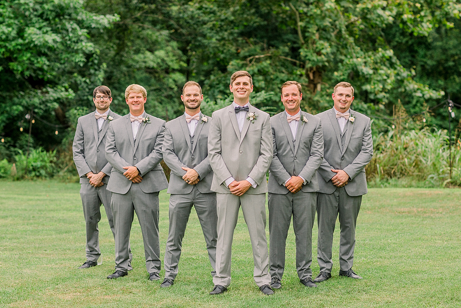 groom poses with groomsmen in grey suits at Creekside Meadows