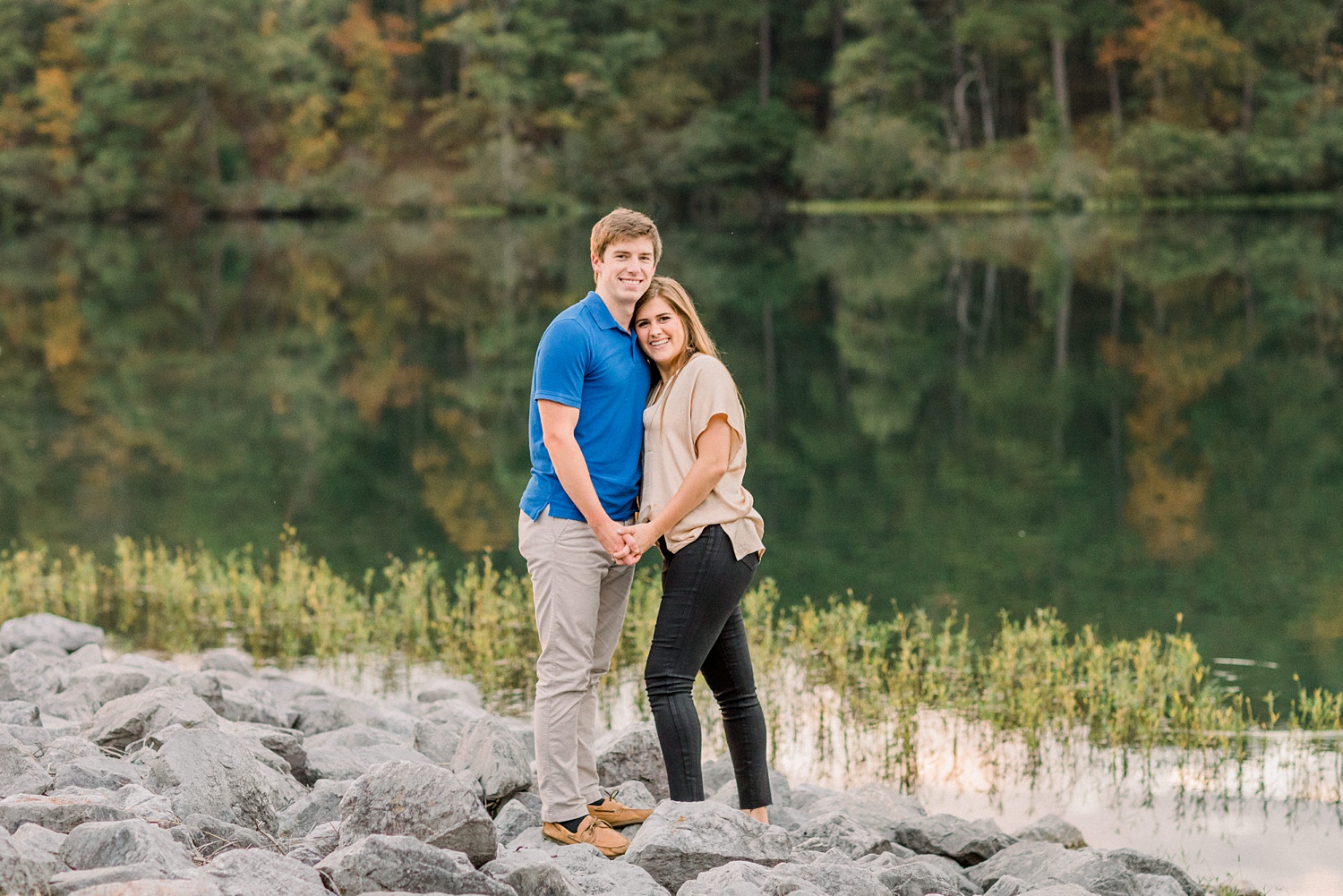 engaged couple stands on rocks by river at Oak Mountain State Park