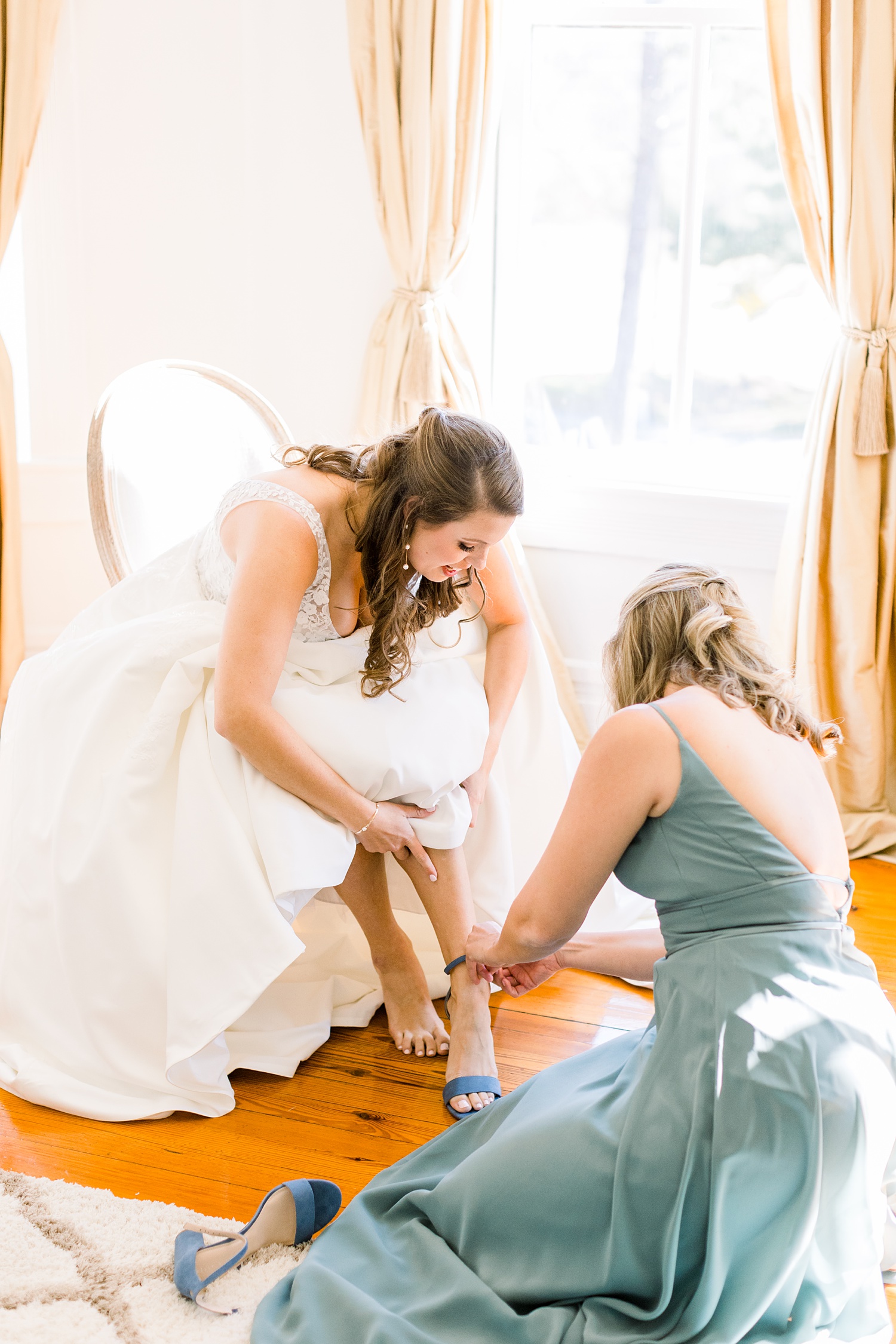 bridesmaid in olive green dress helps bride into shoes