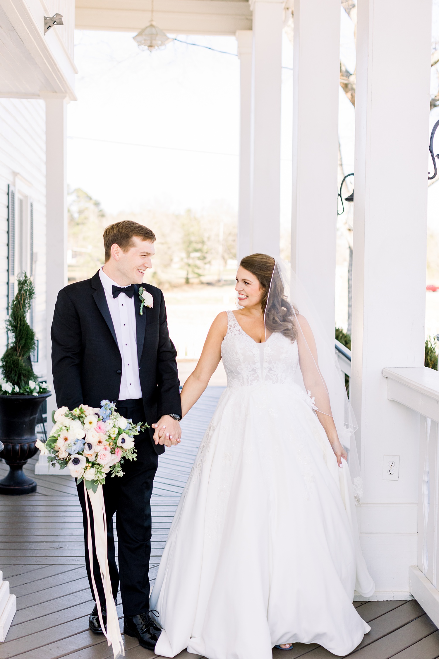 bride and groom hold hands walking on veranda