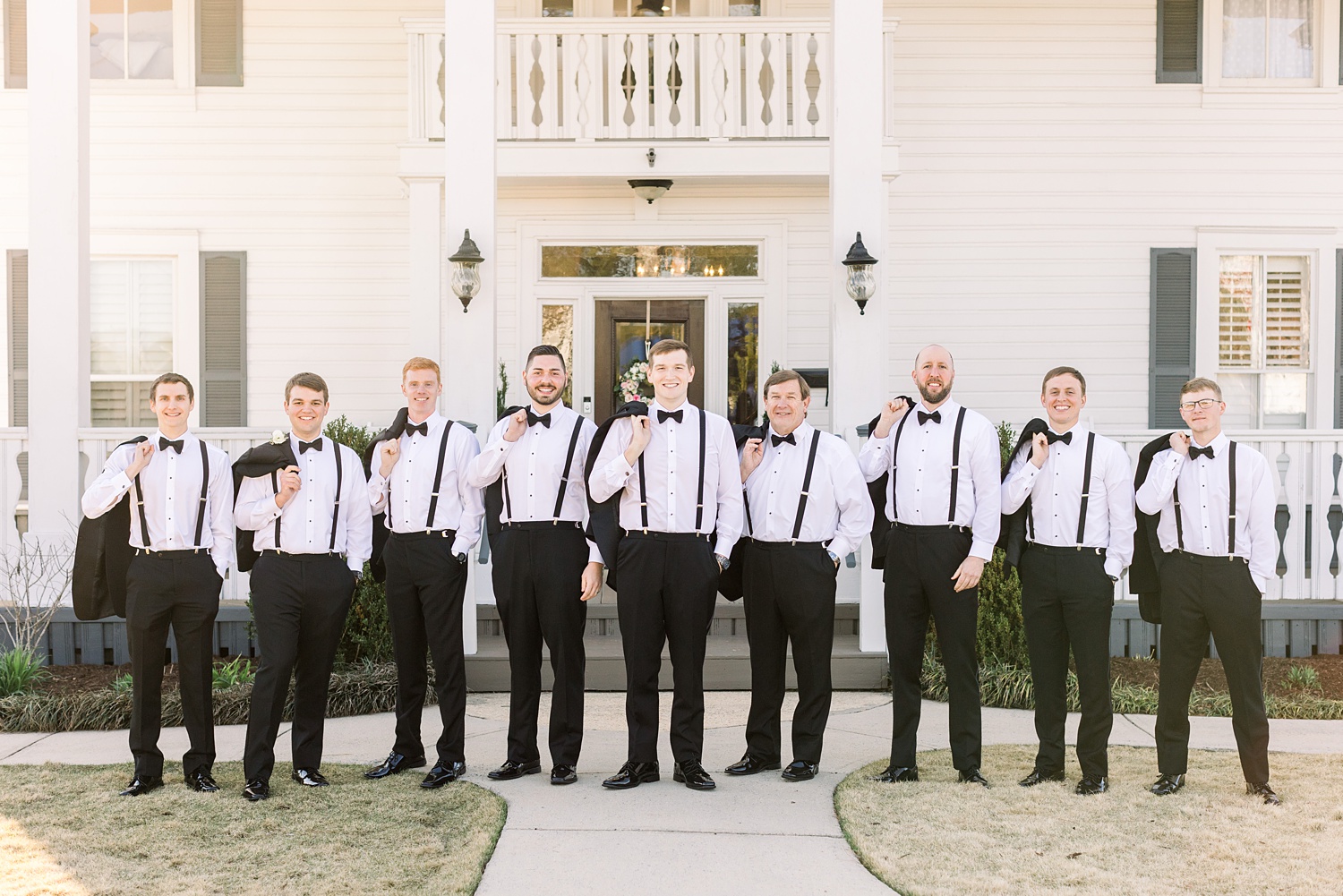 groom poses with groomsmen with jackets off and over their shoulders