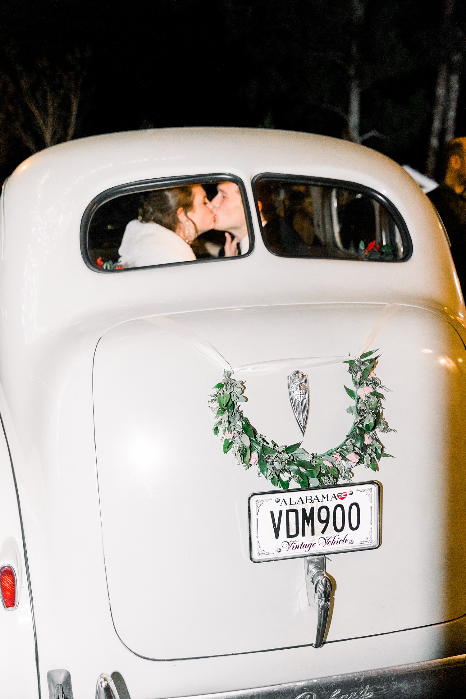 bride and groom kiss in classic getaway car