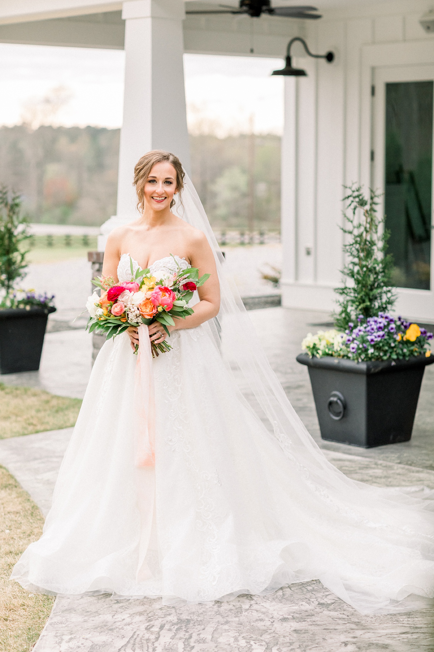 bride holds bouquet of pink and peach flowers outside Oak Meadow Event Center