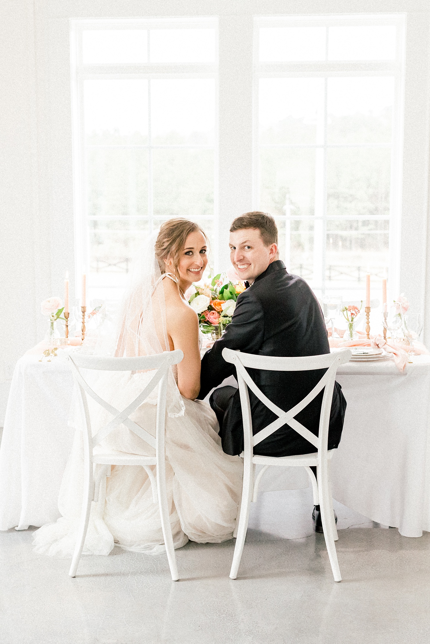 bride and groom sit at reception table looking over shoulder