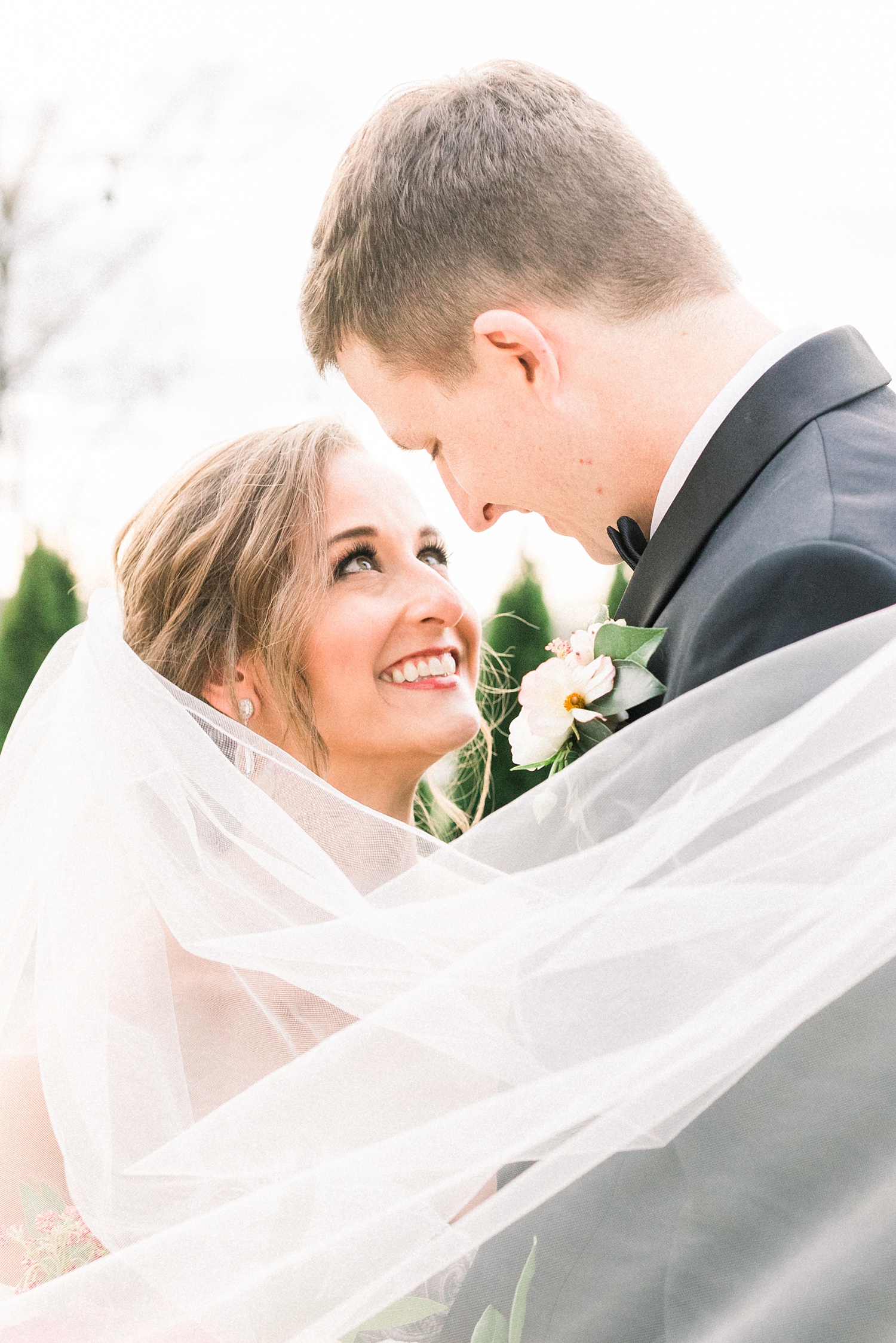 bride looks up at groom with veil draped around shoulders