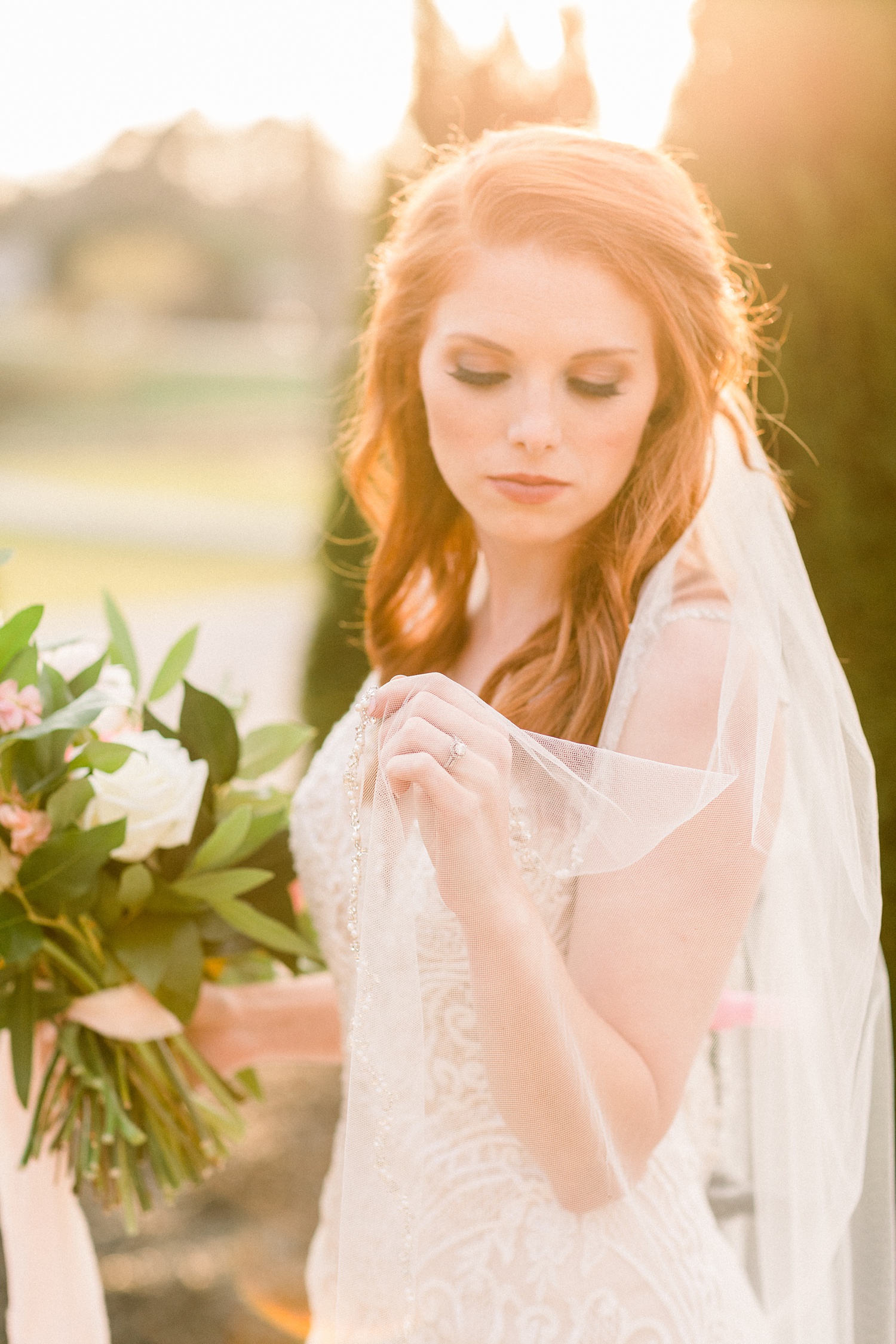 sun-drenched bridal portrait with bride holding edge of veil around shoulders