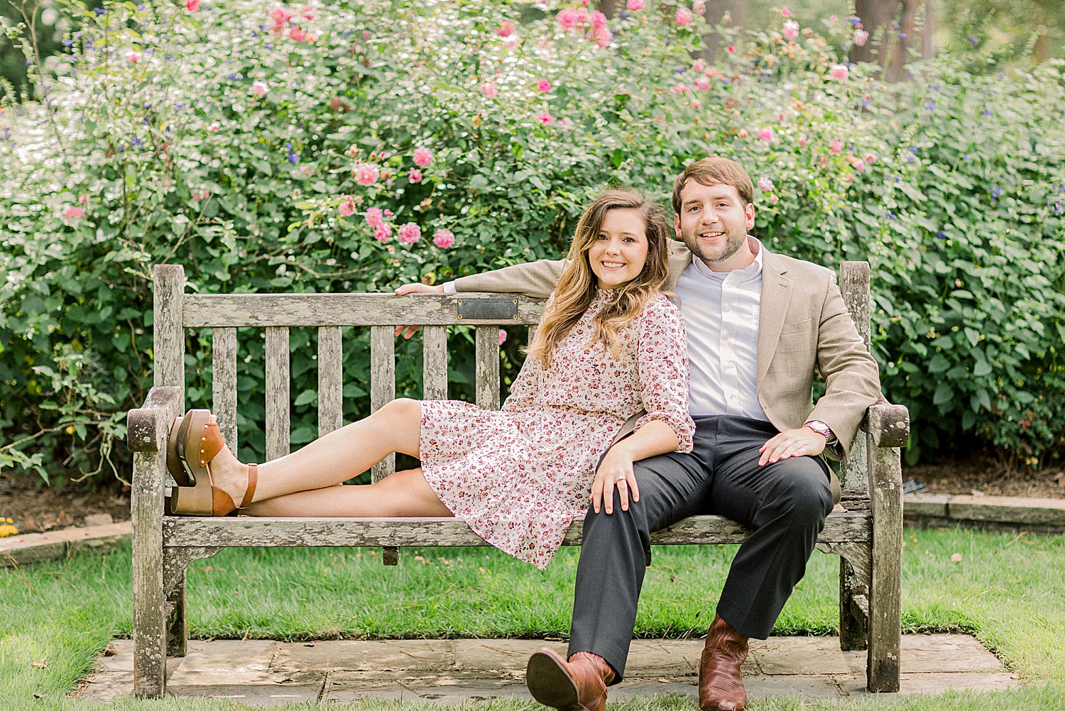 engaged couple sits on wooden bench in Birmingham Botanical Gardens