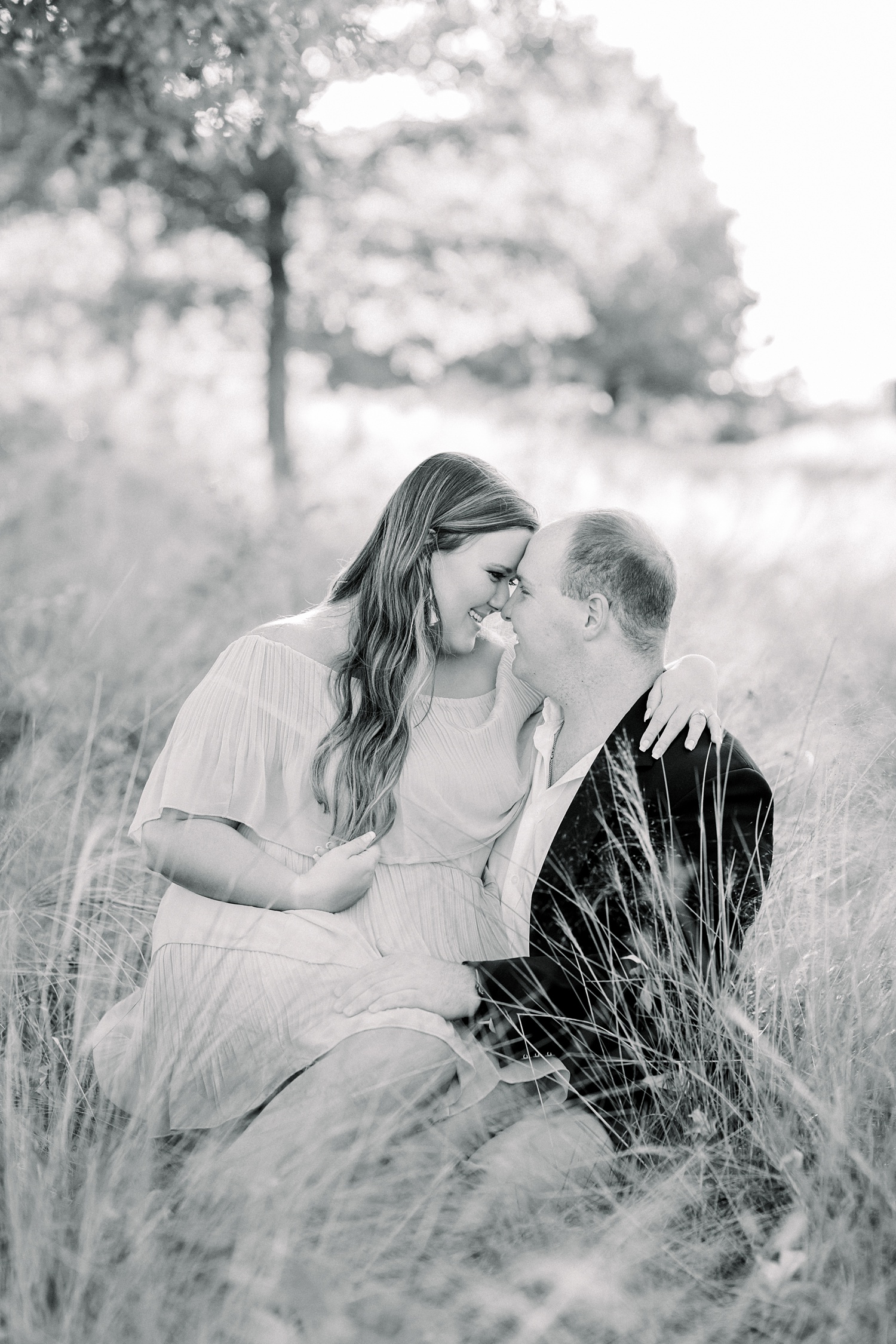 engaged couple sits in field during Downtown Birmingham engagement session