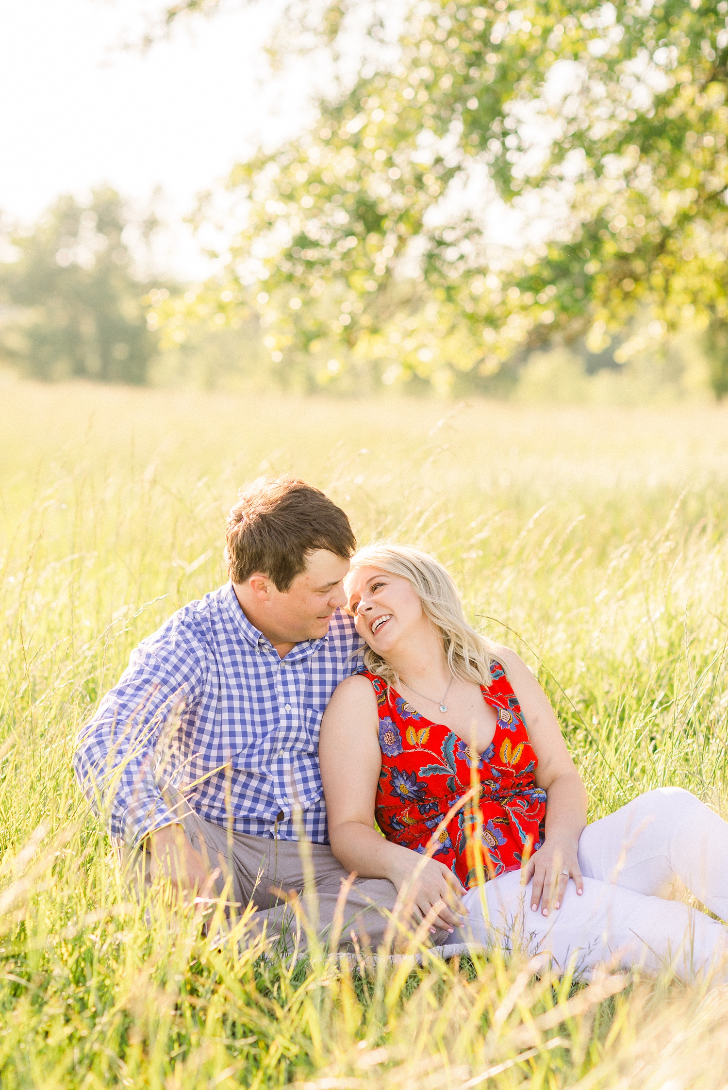 bride leans against groom sitting in grass laughing