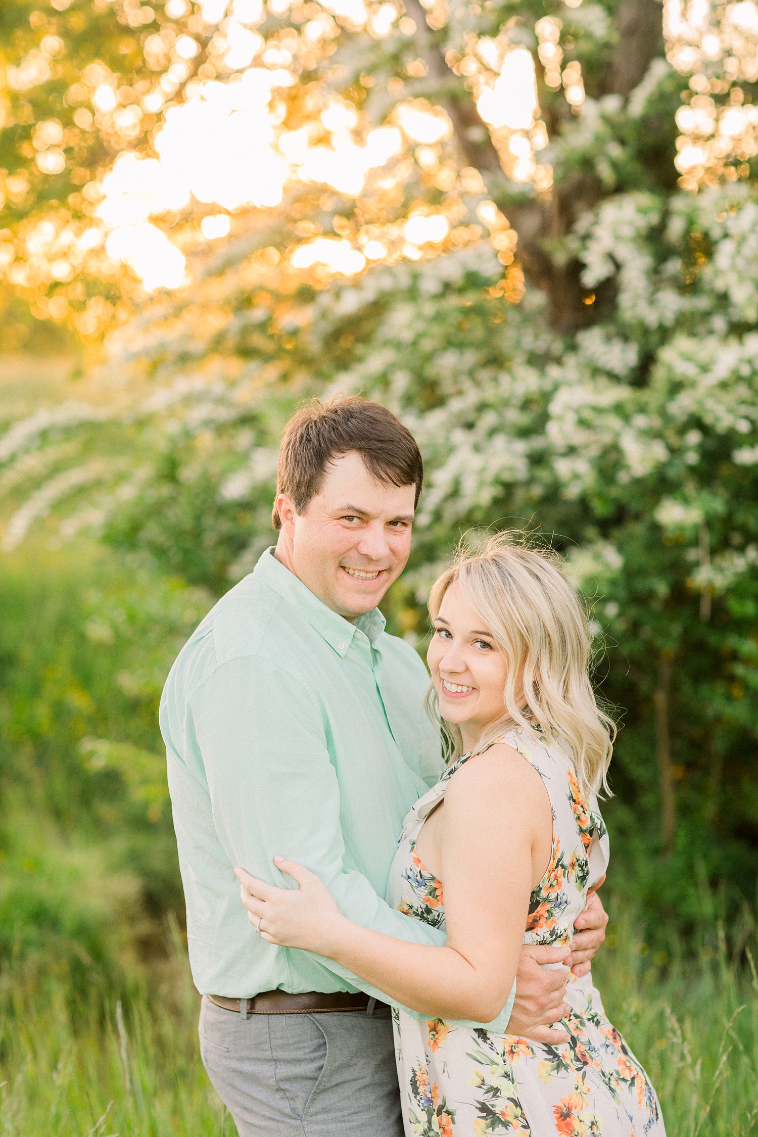 bride and groom pose by tree with white flowers during Huntsville Alabama engagement photos
