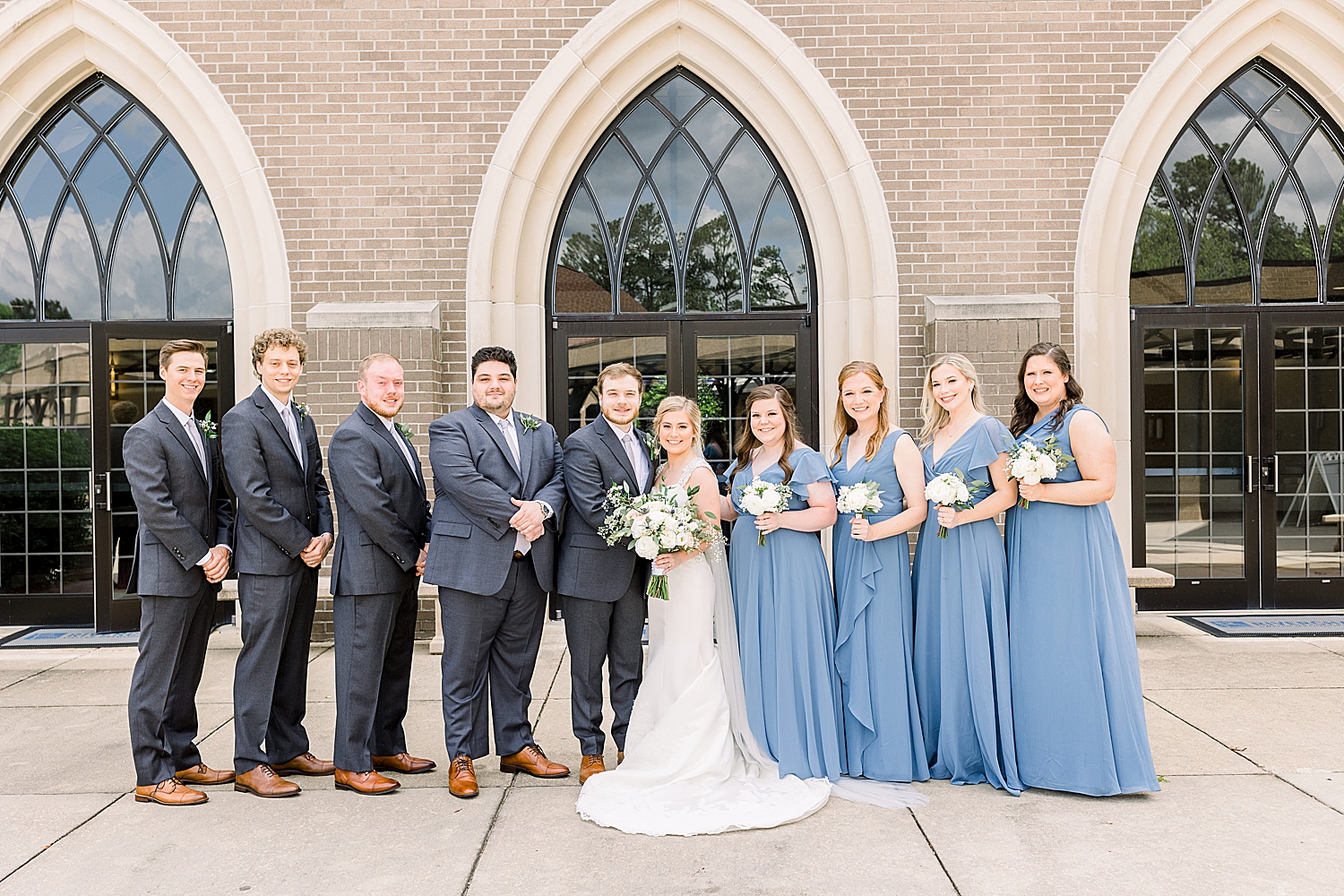 bride and groom pose with bridal party in light blue gowns