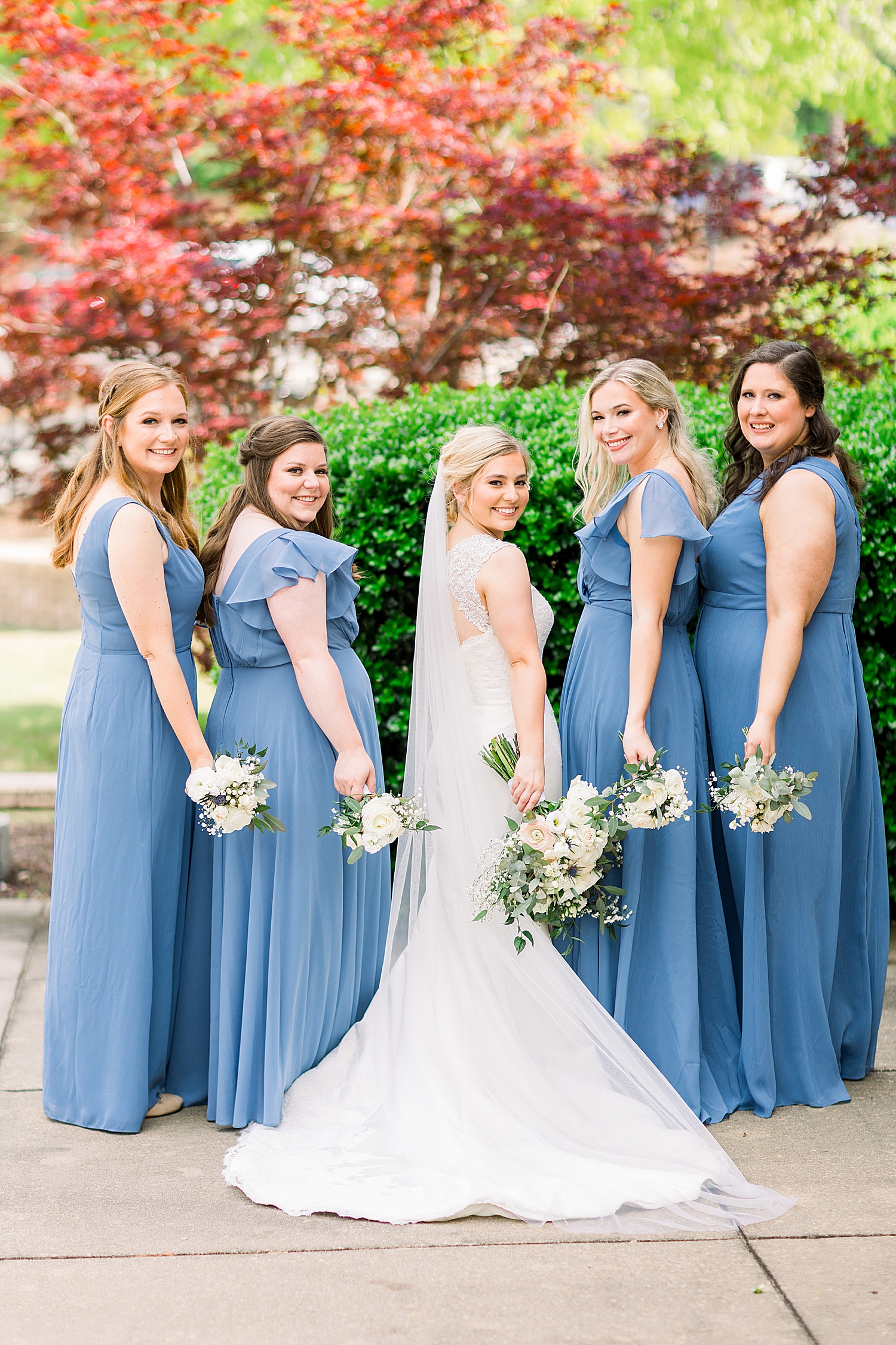 bride poses with bridesmaids in light blue gowns looking over shoulders