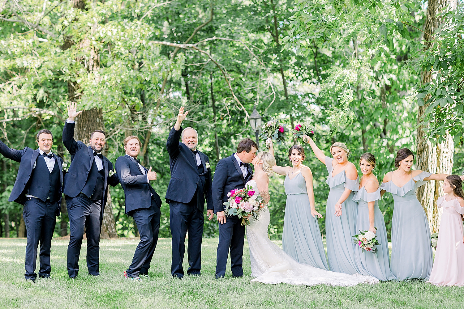 wedding party cheers while bride and groom kiss