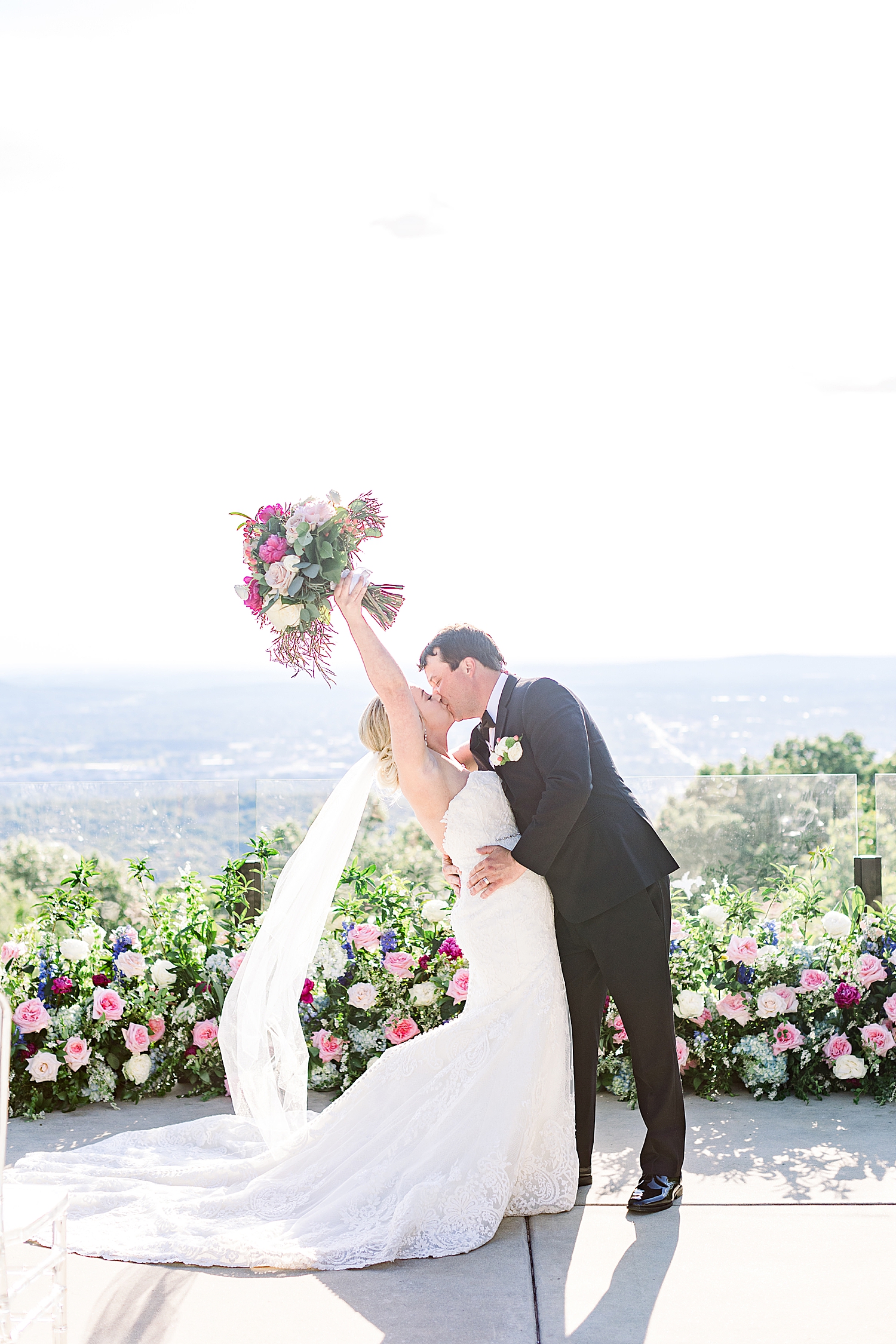 newlyweds kiss while bride holds bouquet in the air
