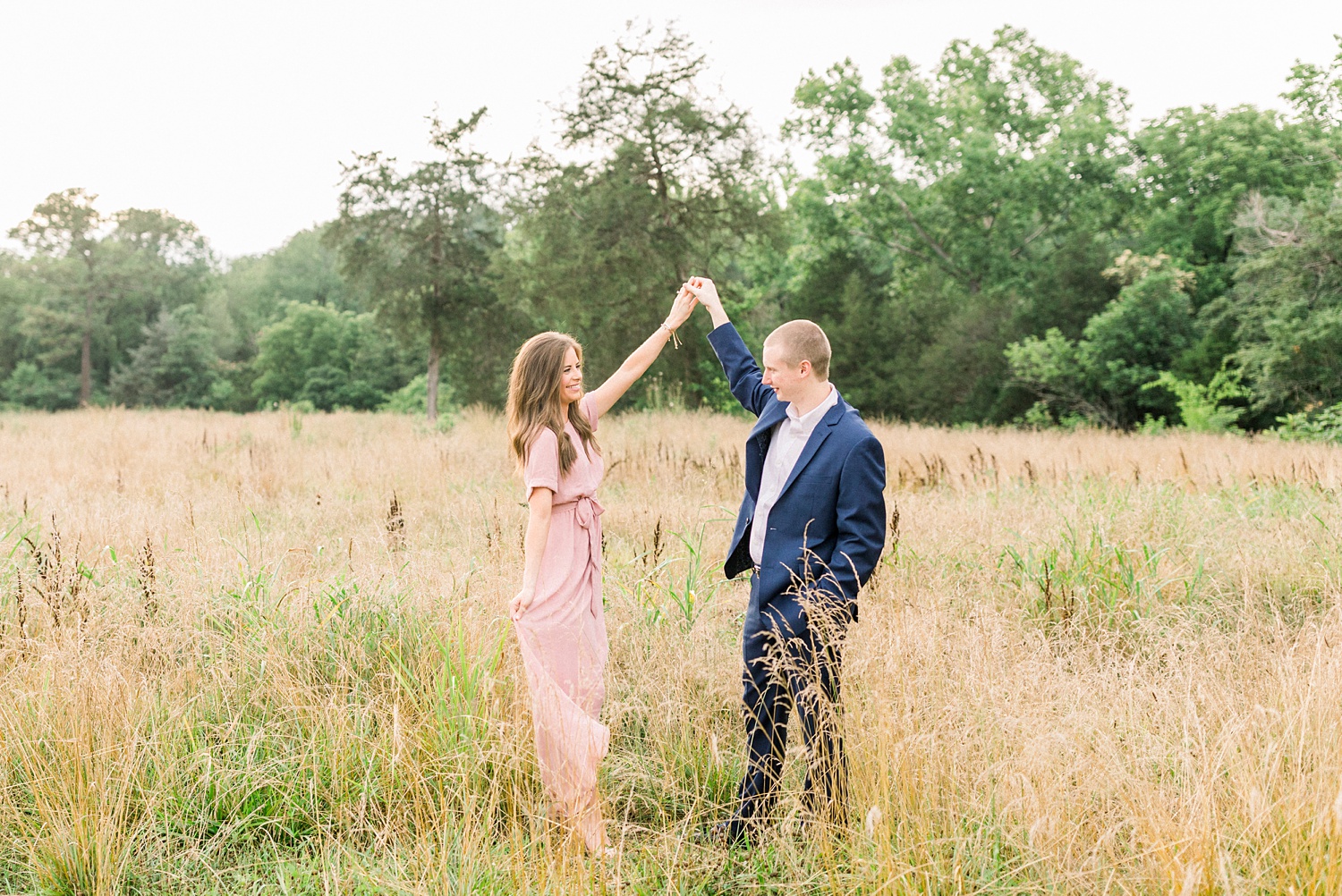 engaged couple dances in field of tall grass