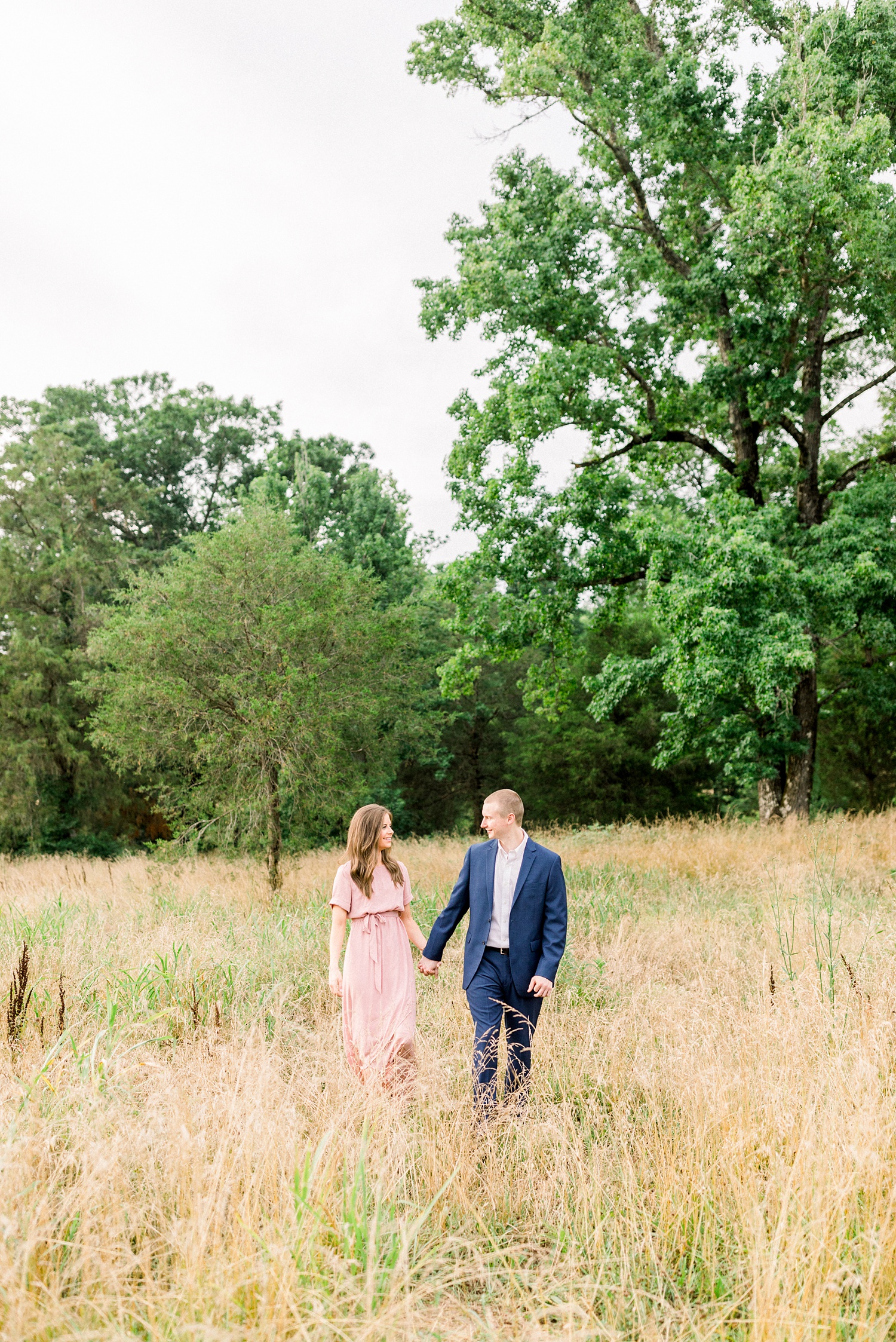 bride and groom walk through field during Montevallo AL engagement session
