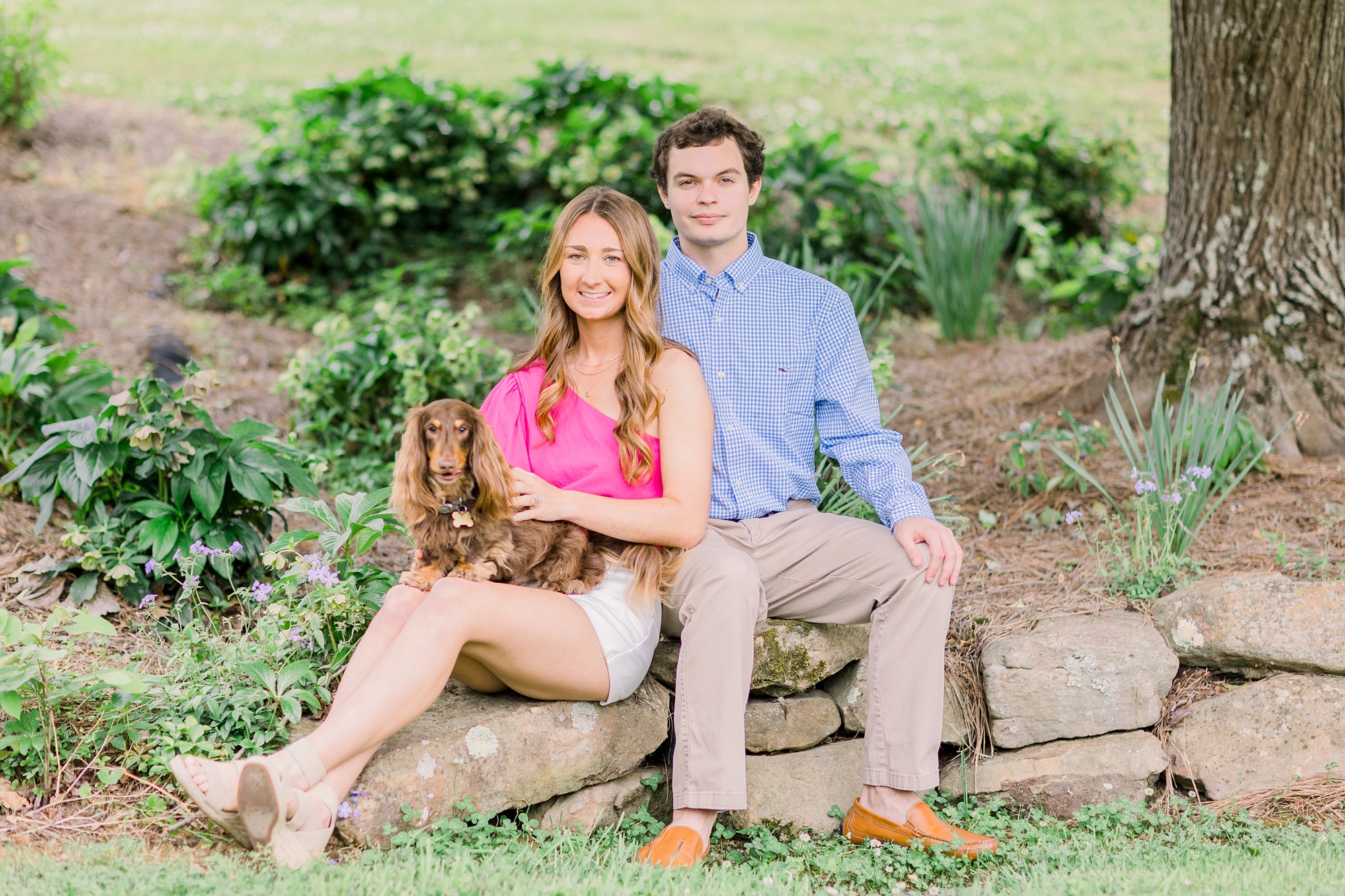 couple poses with dog on rock wall during spring Birmingham AL engagement session