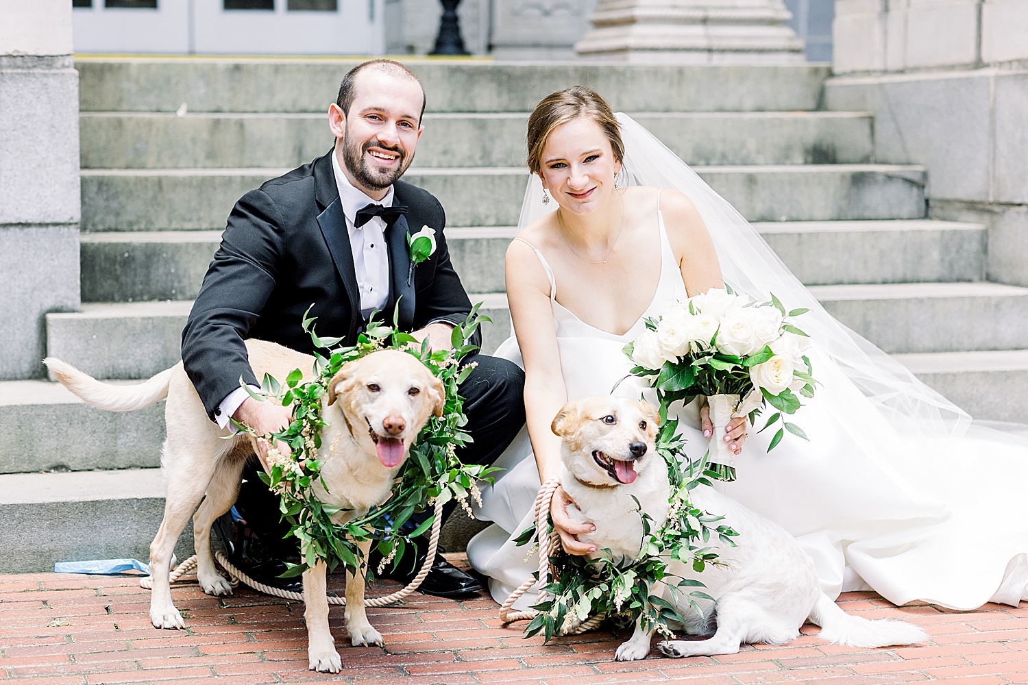 bride and groom pose with two dogs in greenery collars