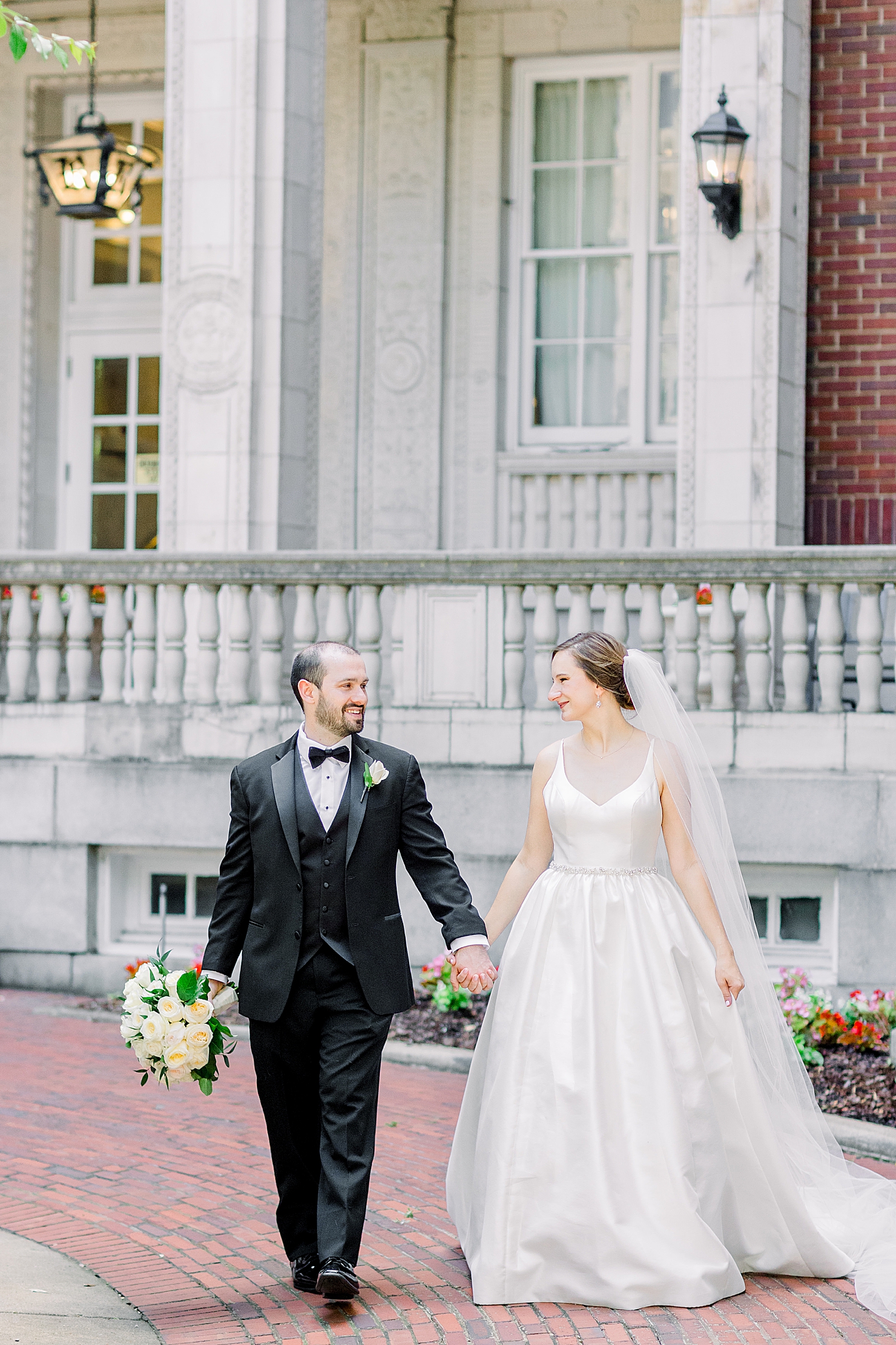 bride and groom hold hands walking outside the Tutwiler Hotel