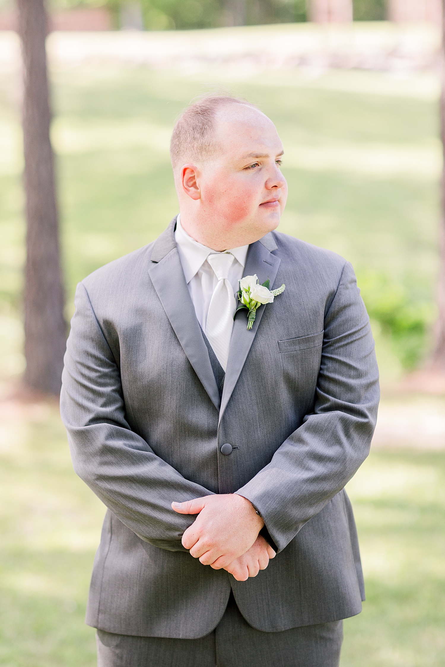 groom stands in grey jacket with hands folded