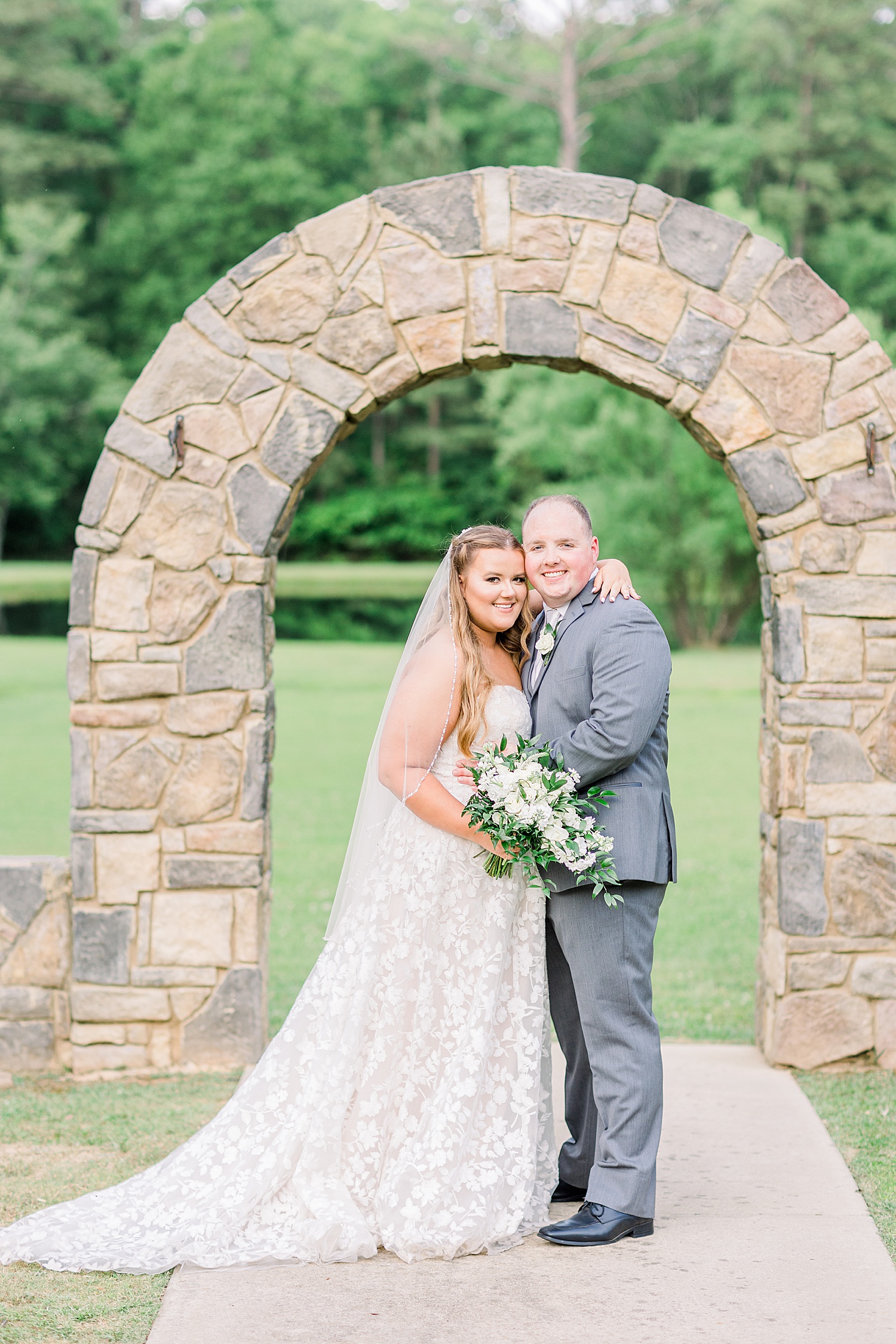 newlyweds stand together under stone arch at Douglas Manor