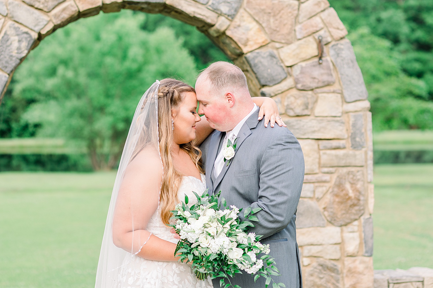 bride and groom nuzzle noses under stone arch