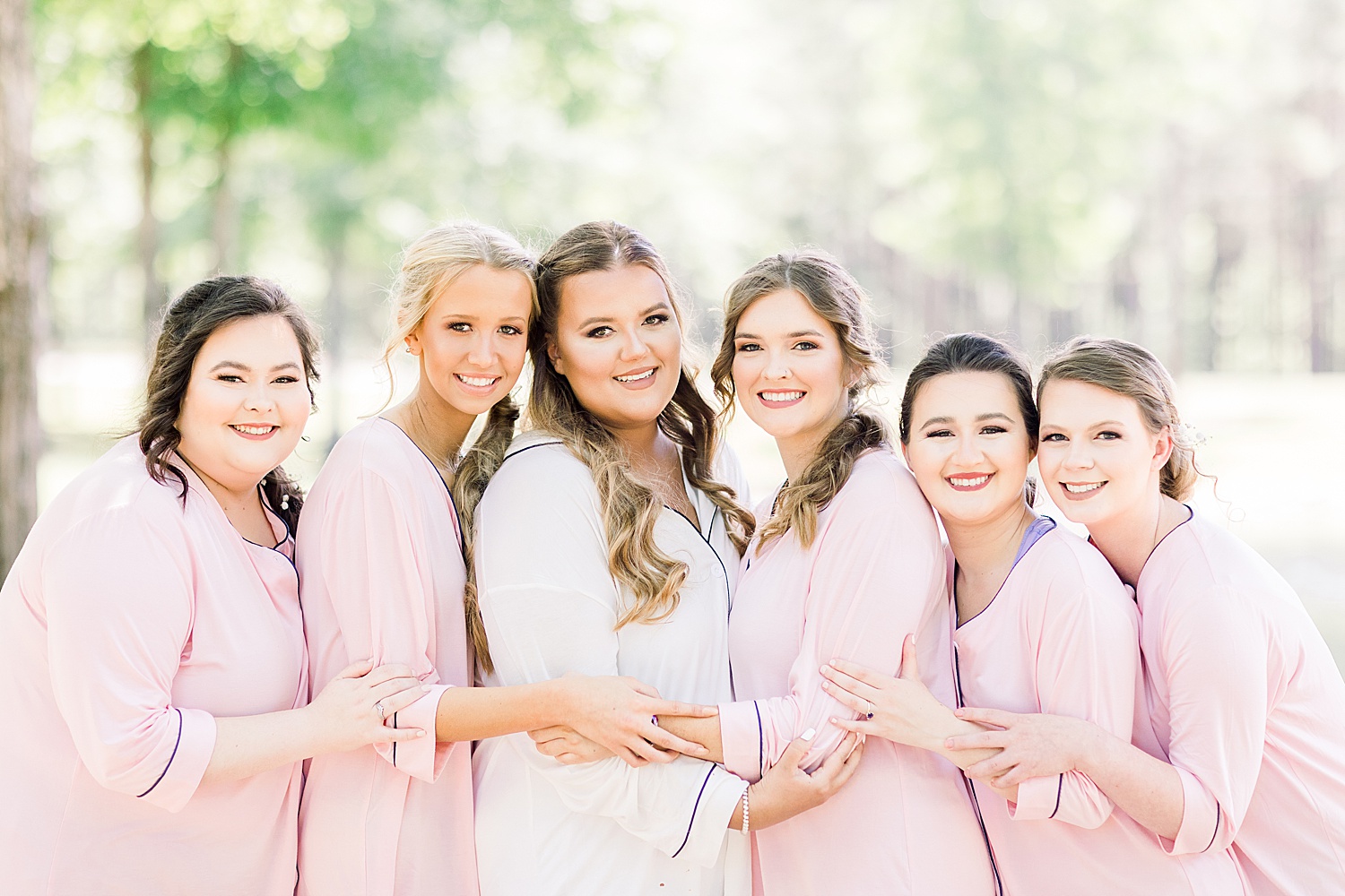 bride and bridesmaids hug in pink robes