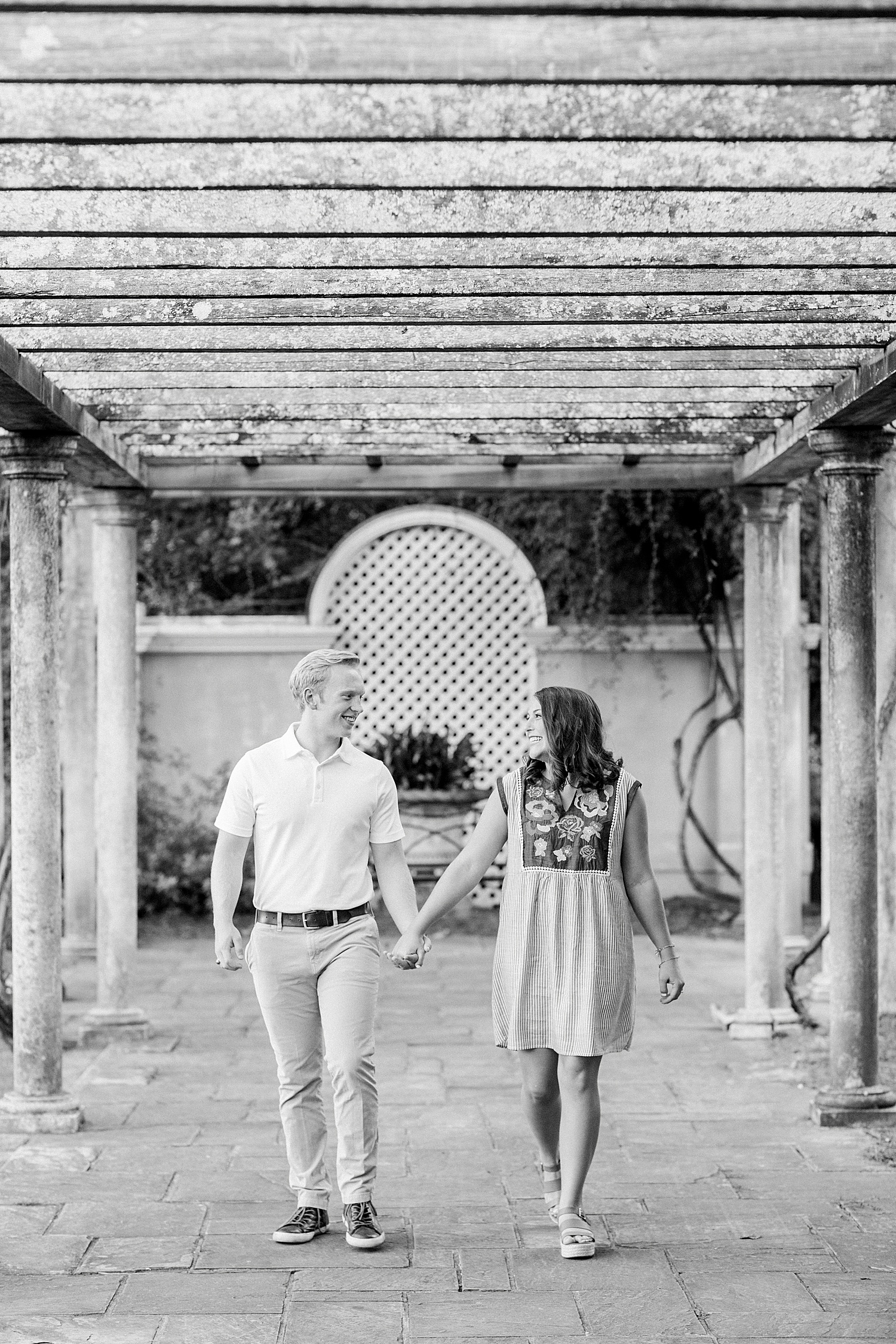 bride and groom hold hands walking under wooden arbor in Birmingham Botanical Gardens
