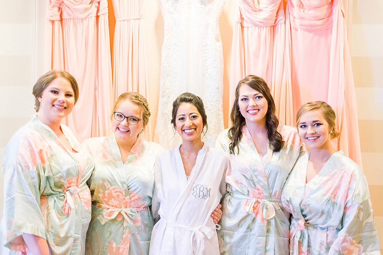 bride and bridesmaids pose together by gowns