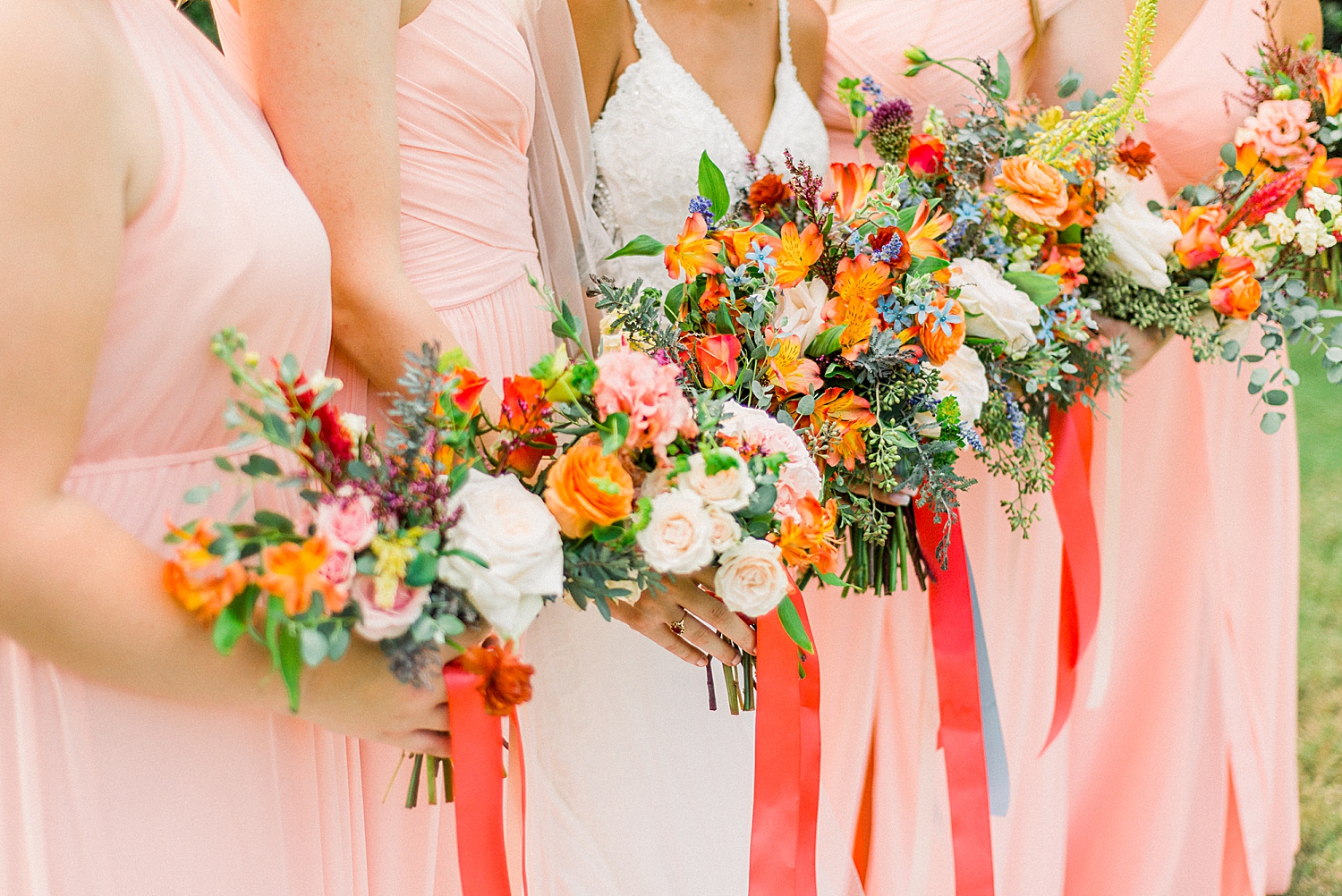 bridesmaids hold bouquets with orange flowers and ribbons