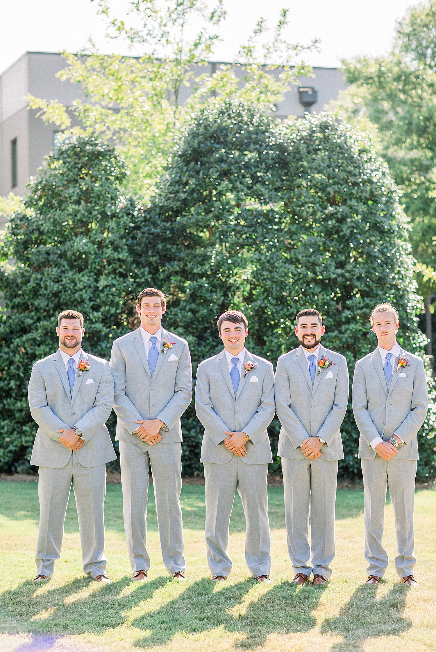 groom and groomsmen pose with hands crossed in grey suits