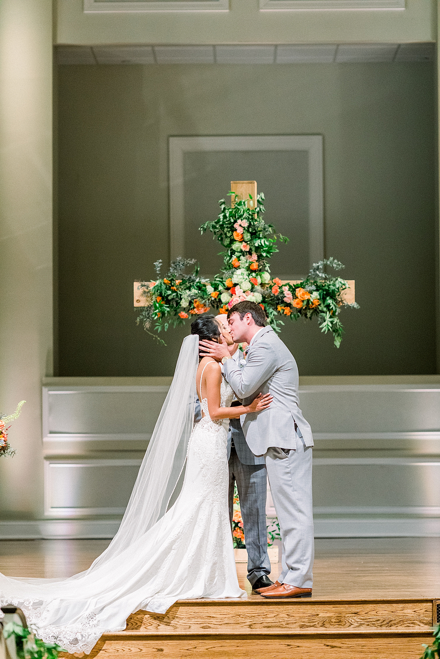 newlyweds kiss by floral covered cross at church wedding