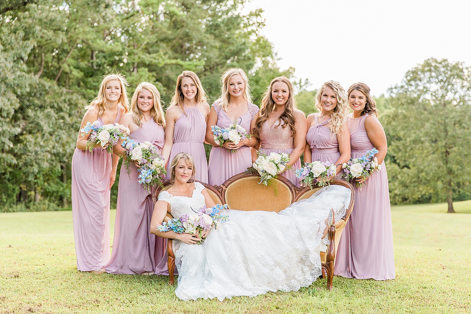 bride lays on couch surrounded by bridesmaids in pink dresses