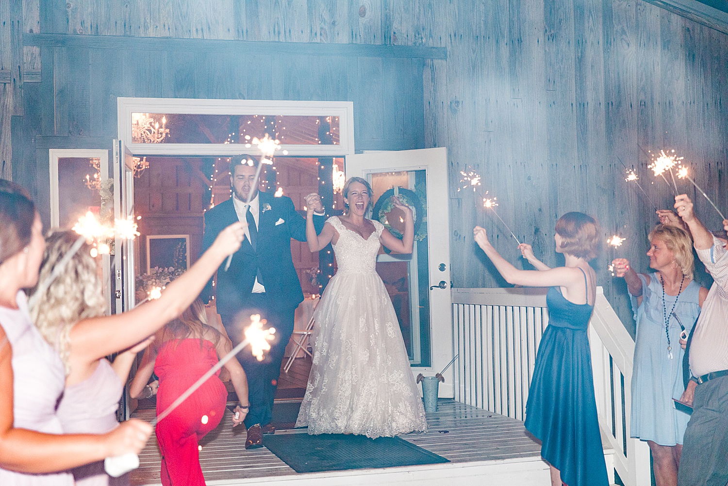 bride and groom walk out of reception barn as guests hold sparklers