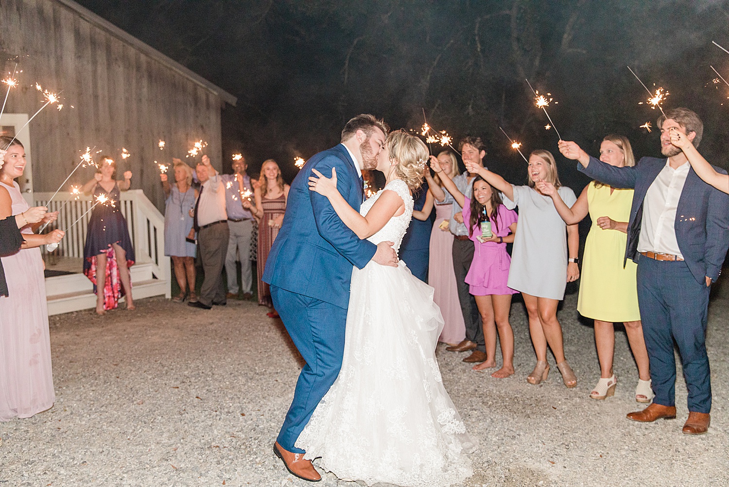 husband and wife kiss at the end of wedding night surrounded by their guests holding sparklers