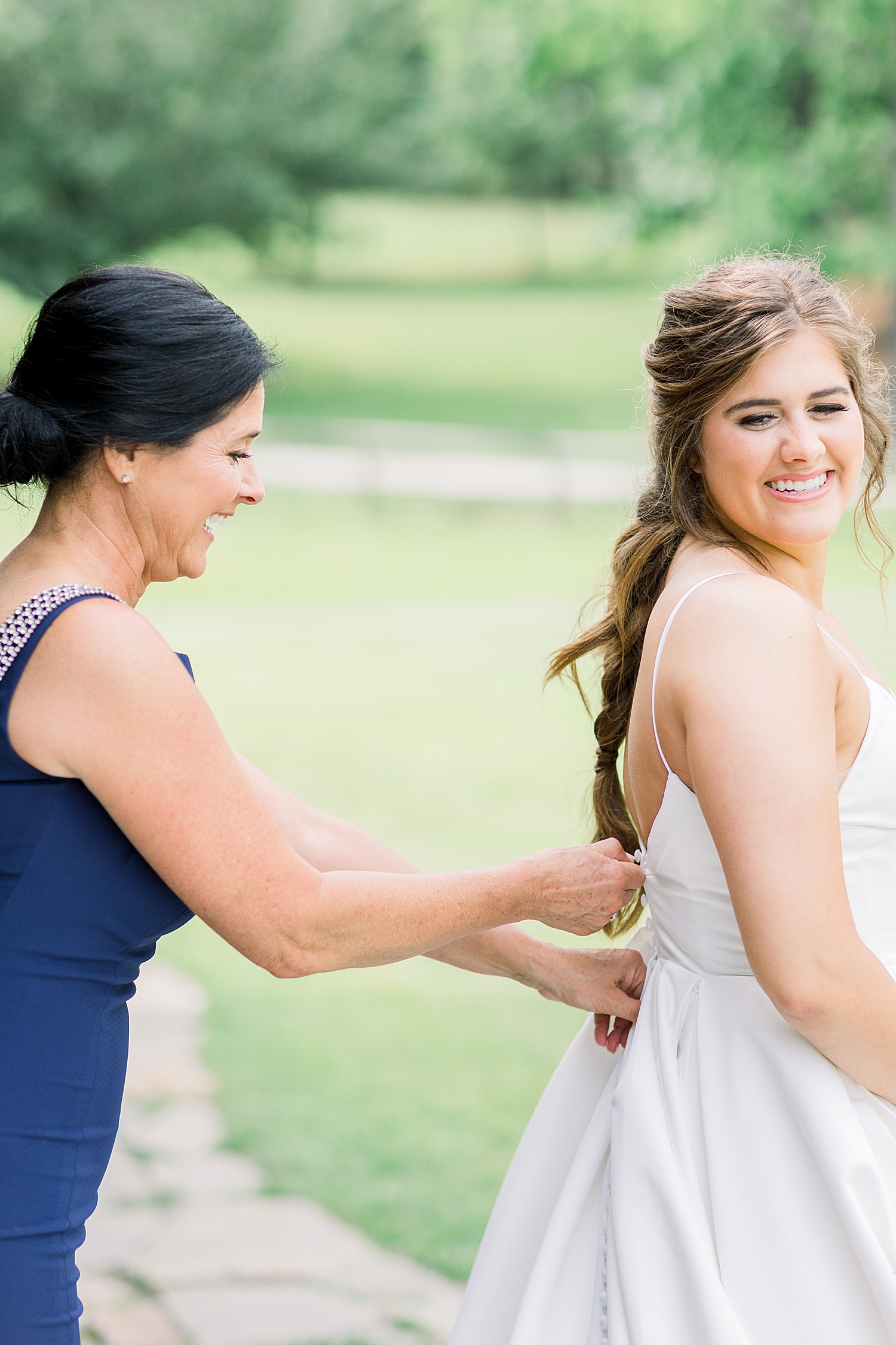 mother of the bride helps fasten back of wedding dress before ceremony