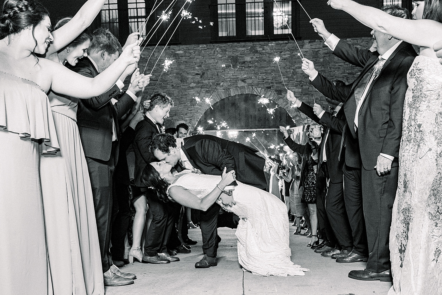 groom dips bride and kisses her as guests hold sparklers