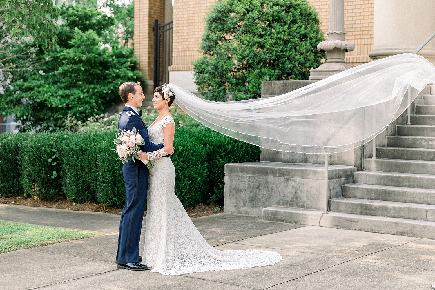 Bride + Groom stand outside in Birmingham Alabama as bride's veil flows behind her