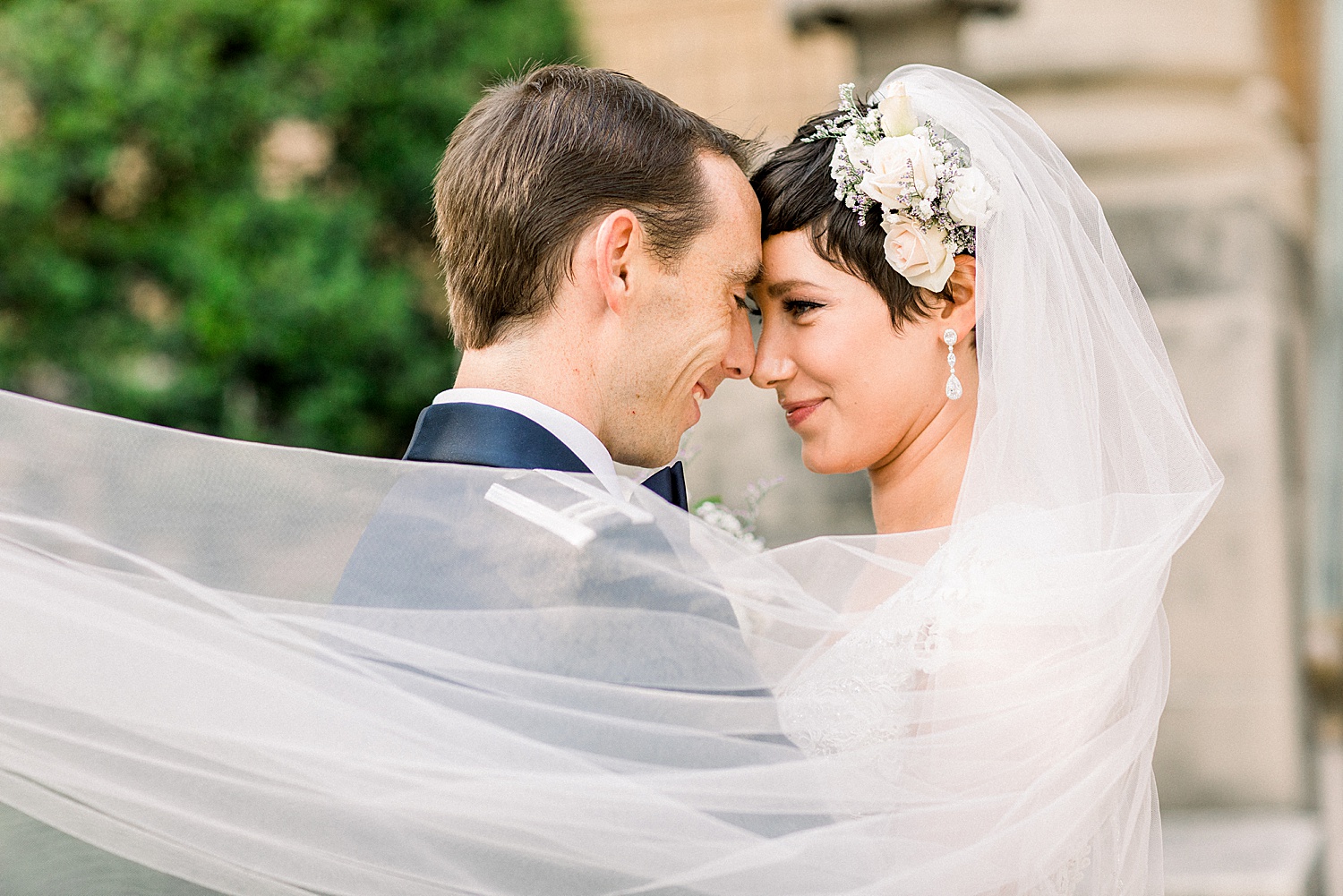 couple leans heads in together as veil wraps around them