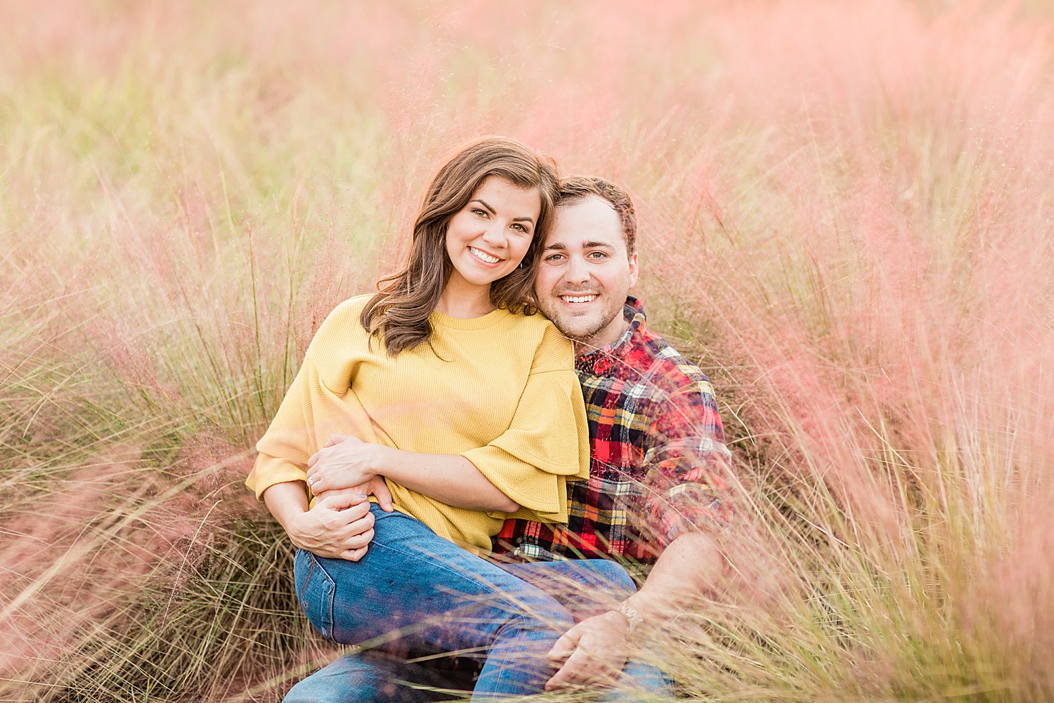 couple sit in the tall pink grass during engagement photos