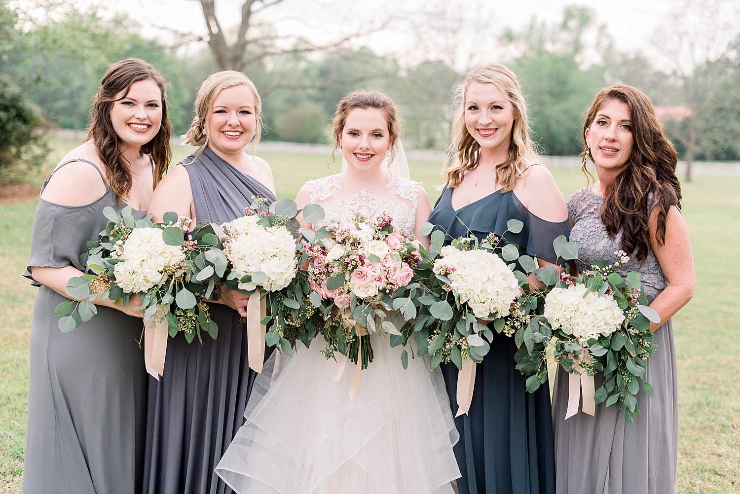 bride and bridesmaids in dark grey hold their wedding bouquets together before AL wedding ceremony