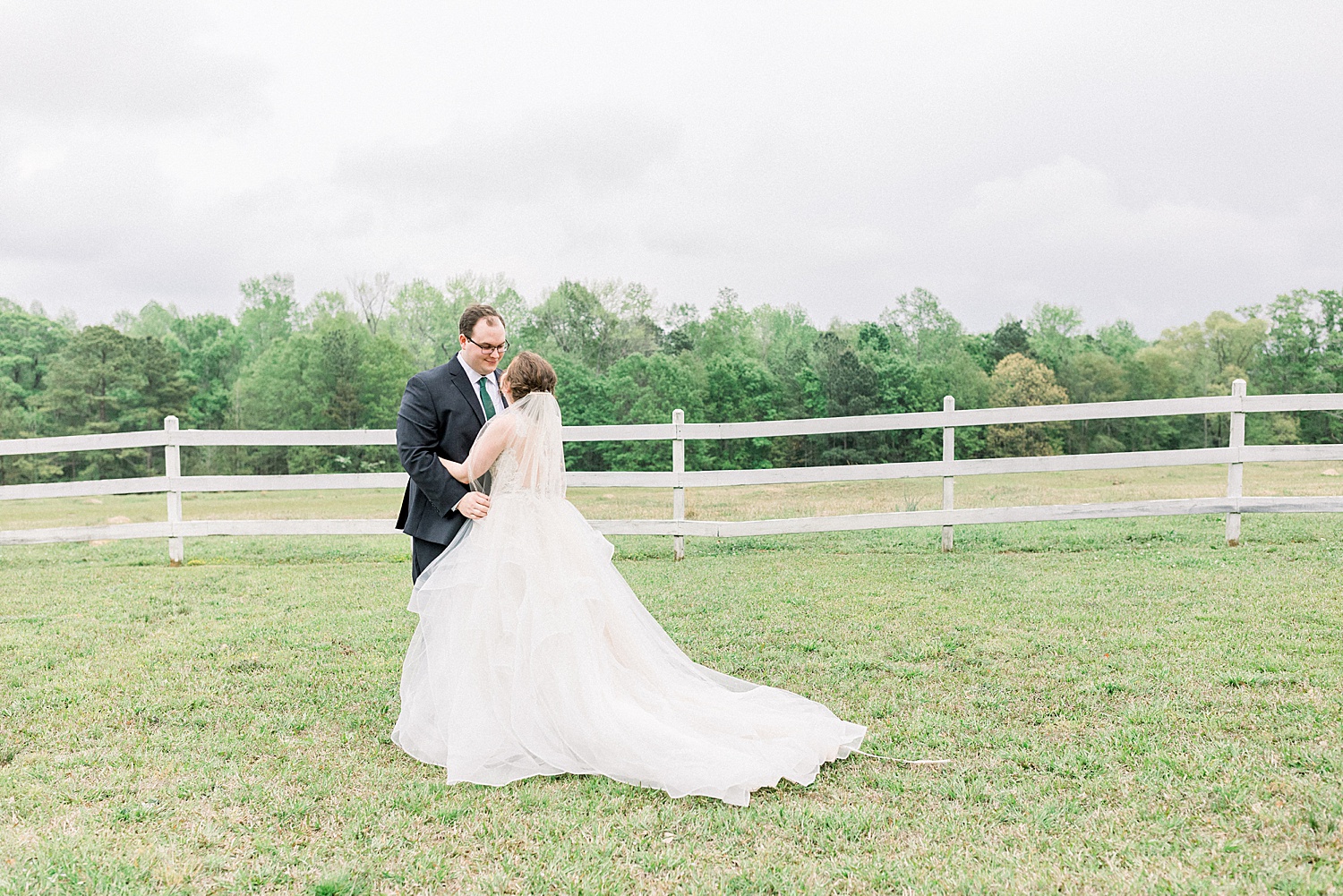 bride and groom during first look in field with white fence